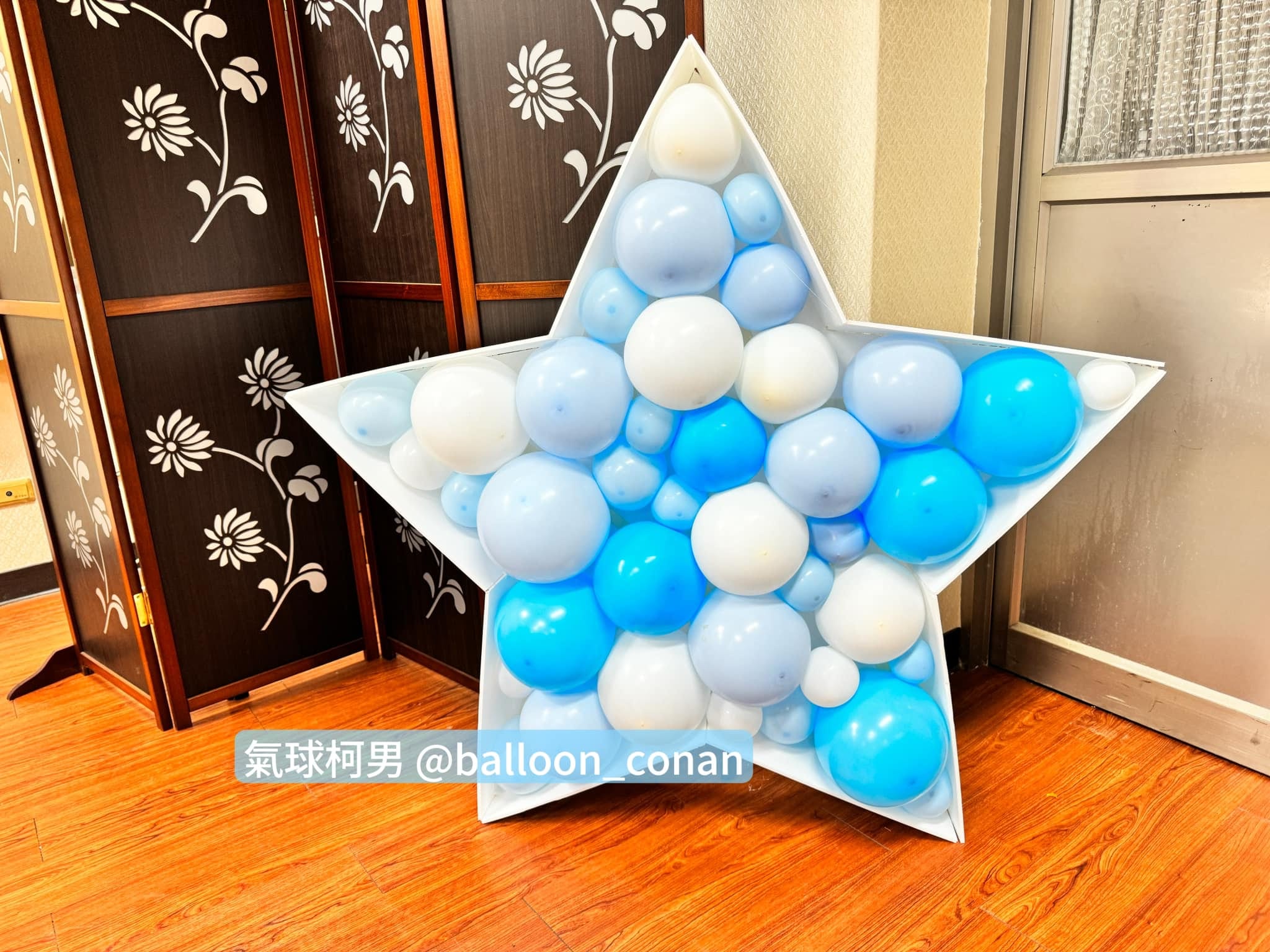 白色星星框內塞滿藍色、淺藍與白色氣球，立在屏風旁的木地板上