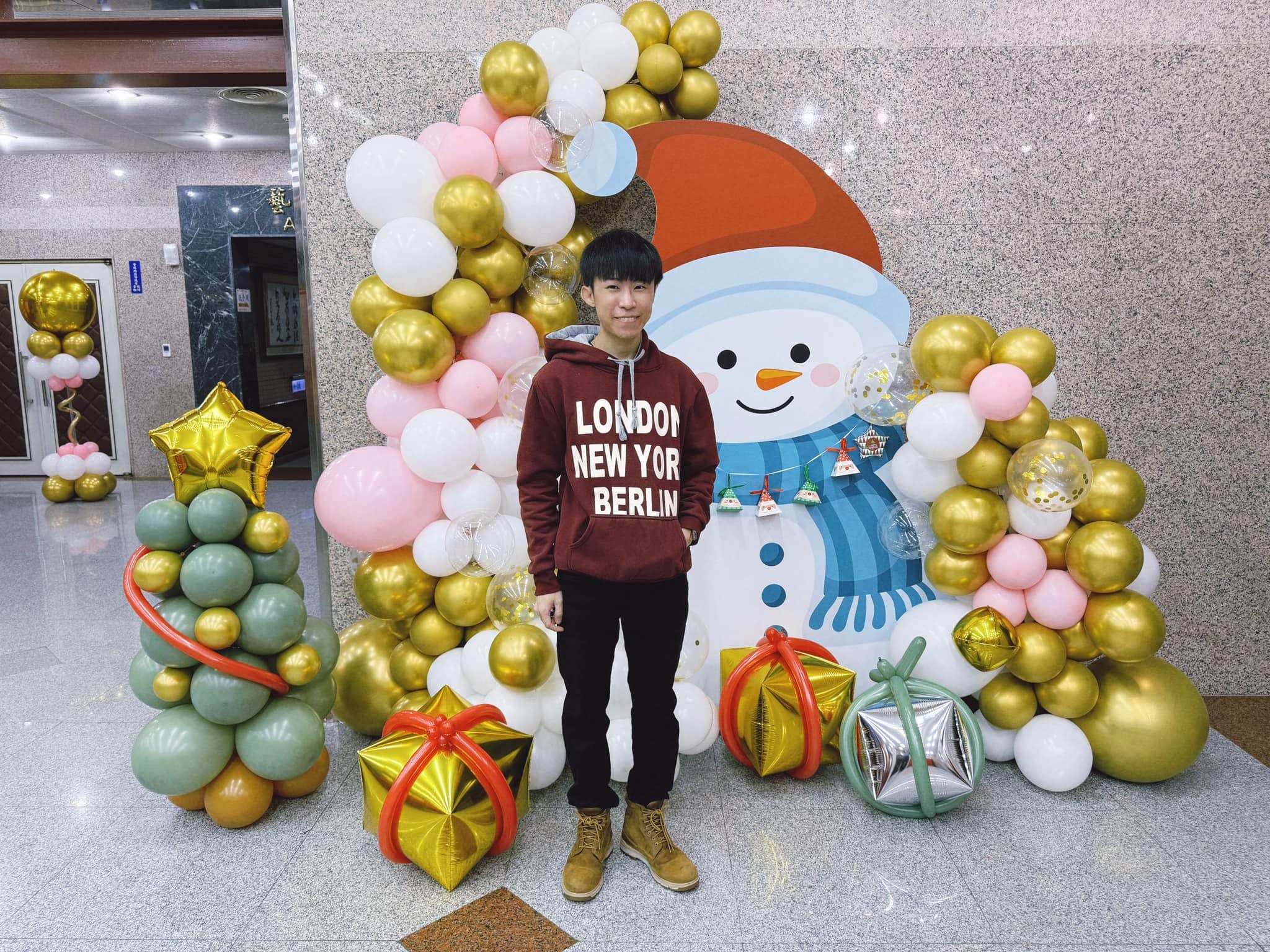 柯男站在雪人背板前，兩側是金色與粉色氣球串