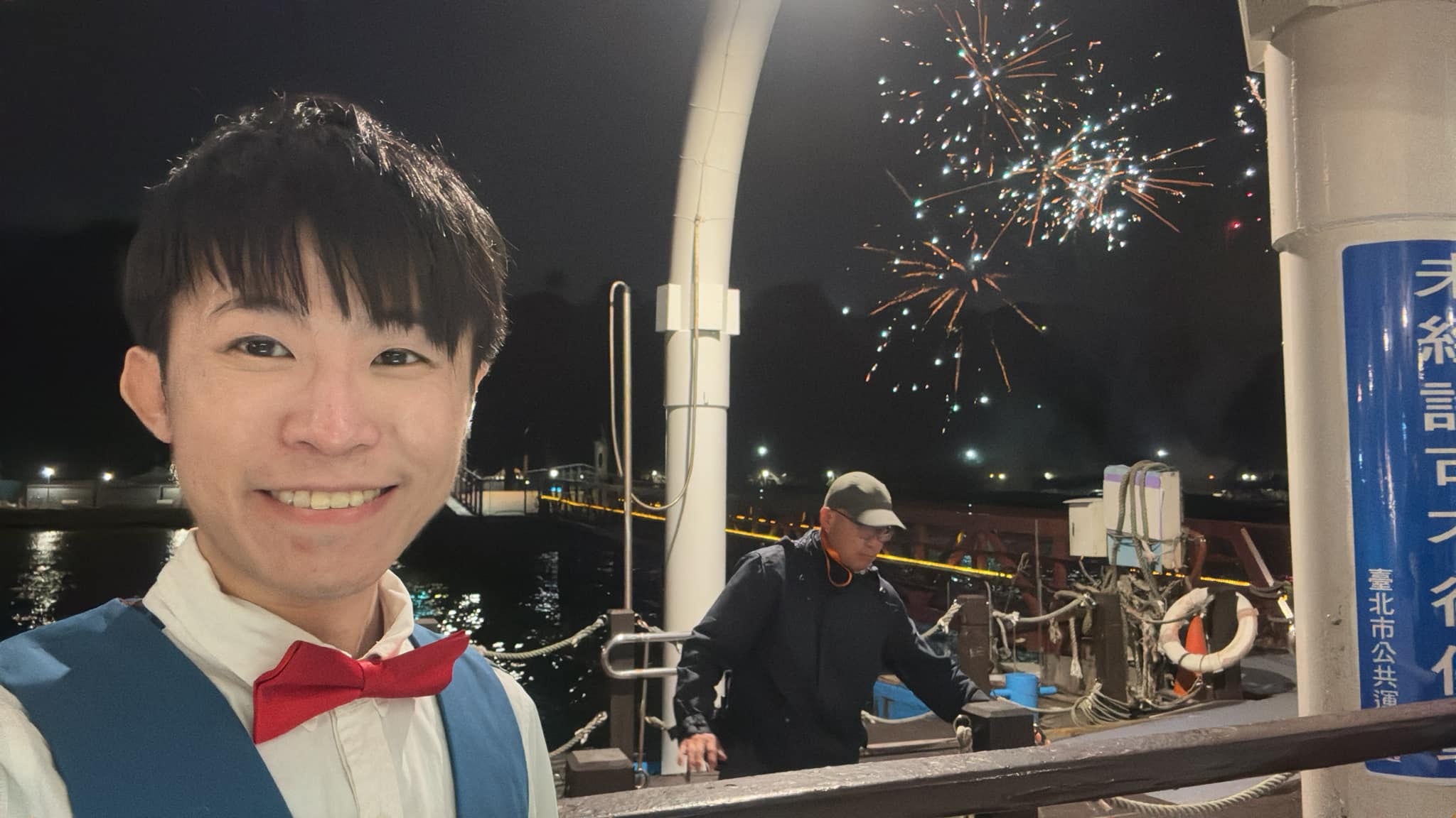夜晚的碼頭邊，柯男自拍，身後河面上空綻放煙火