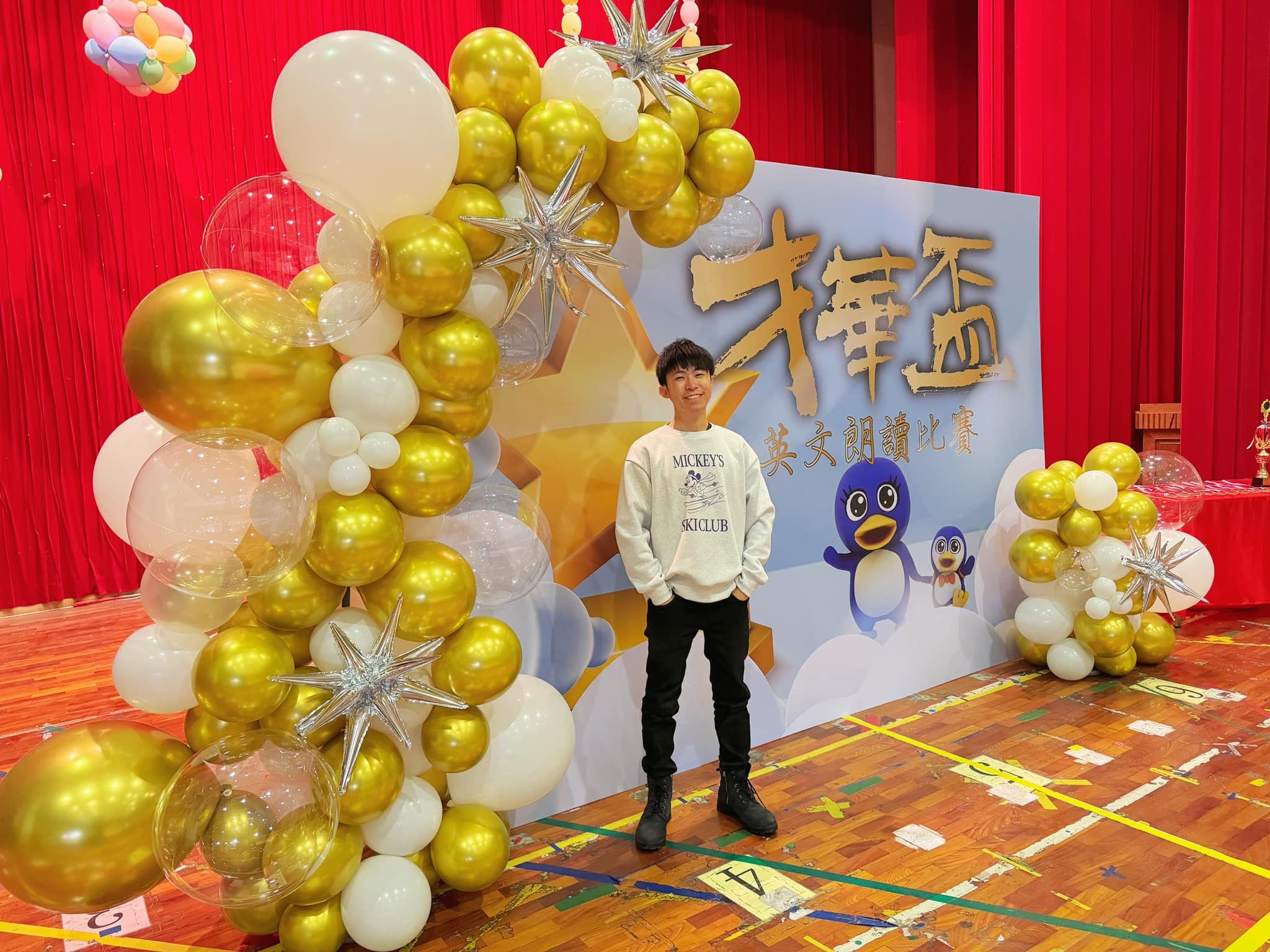 台中霧峰英文朗讀比賽舞台，柯男站在金白氣球串與星星背板前