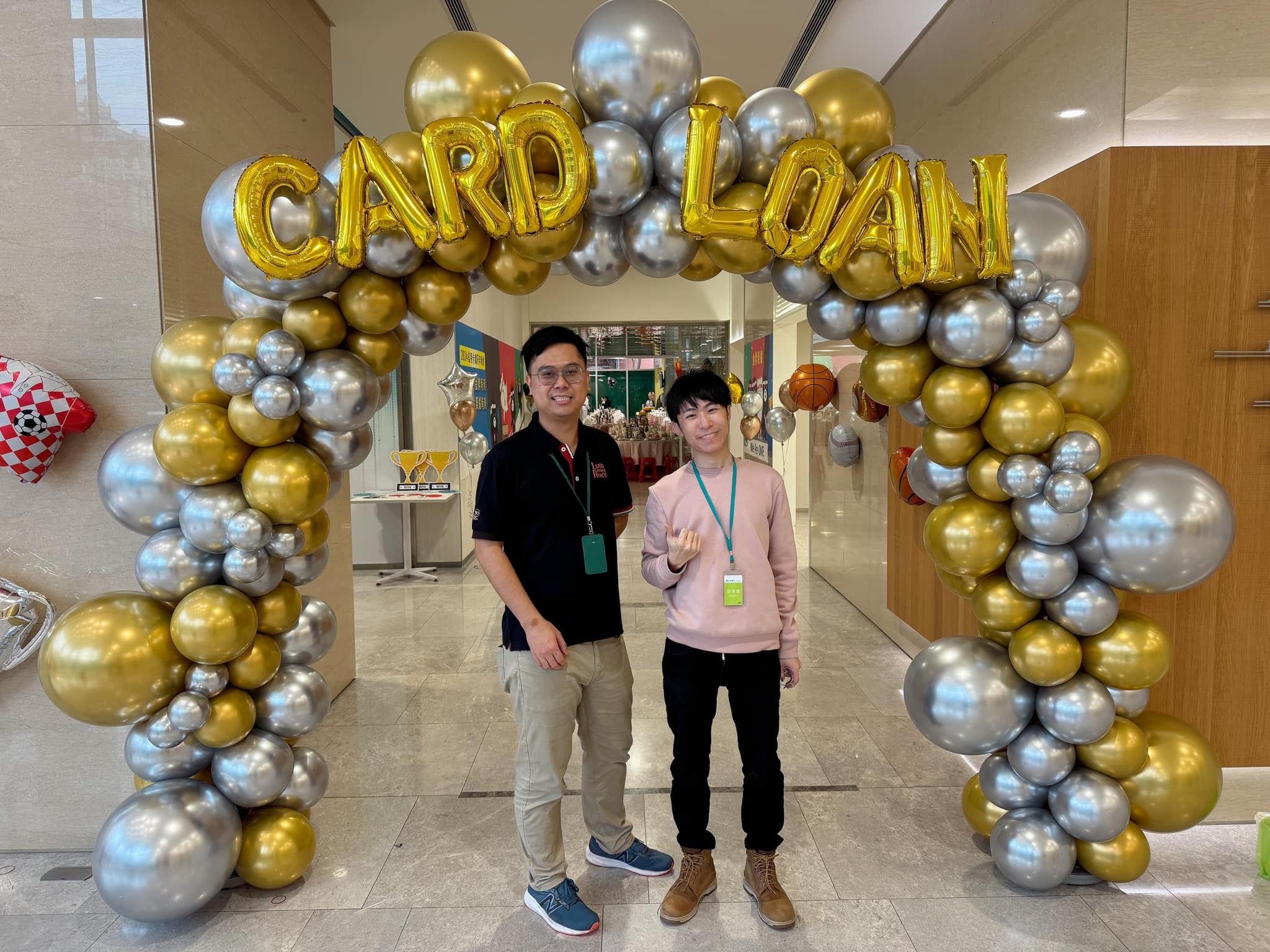 金銀氣球拱門下，穿黑色上衣與粉色上衣的兩人合照