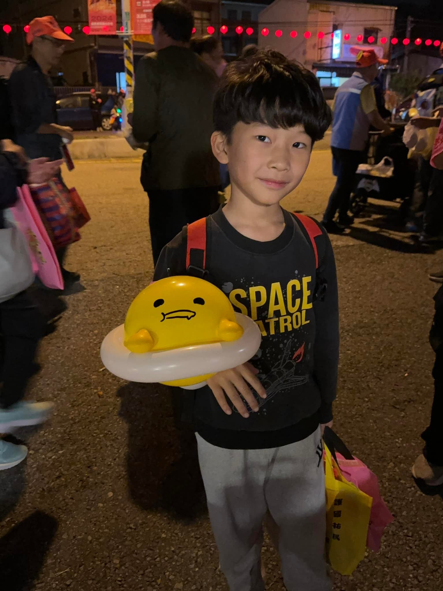 夜晚進香路上，男孩抱著趴在蛋白上的蛋黃哥氣球