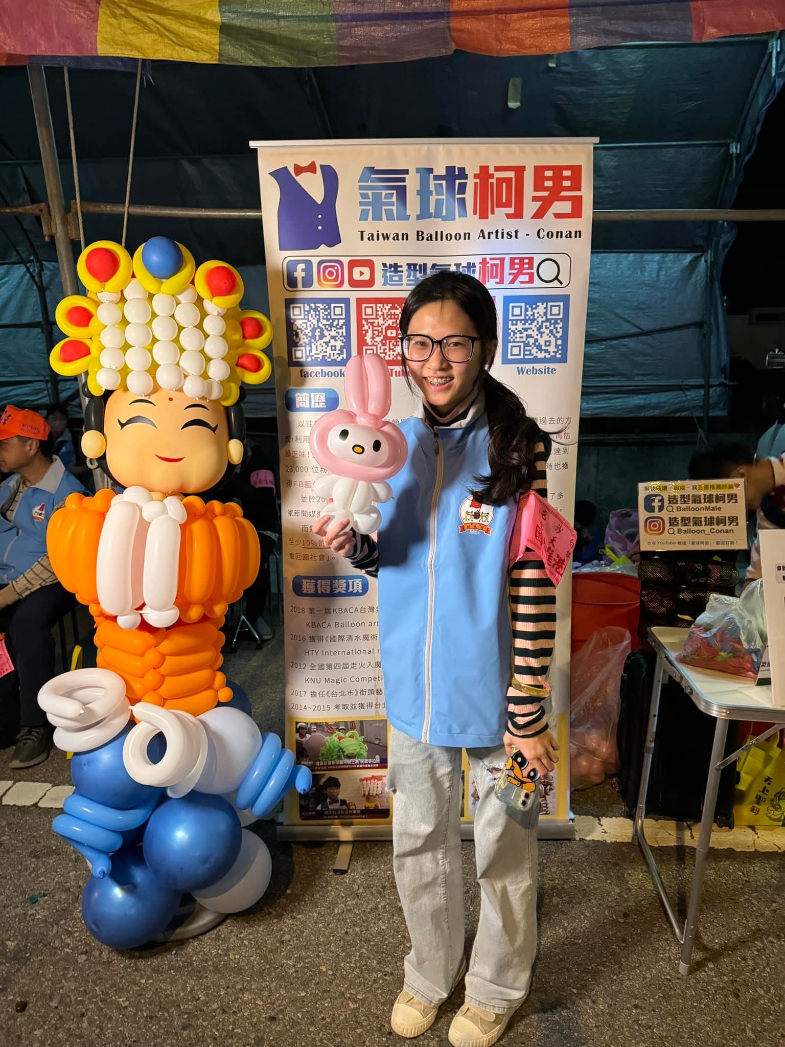 穿淺藍背心的少女拿著美樂蒂氣球站在媽祖氣球旁