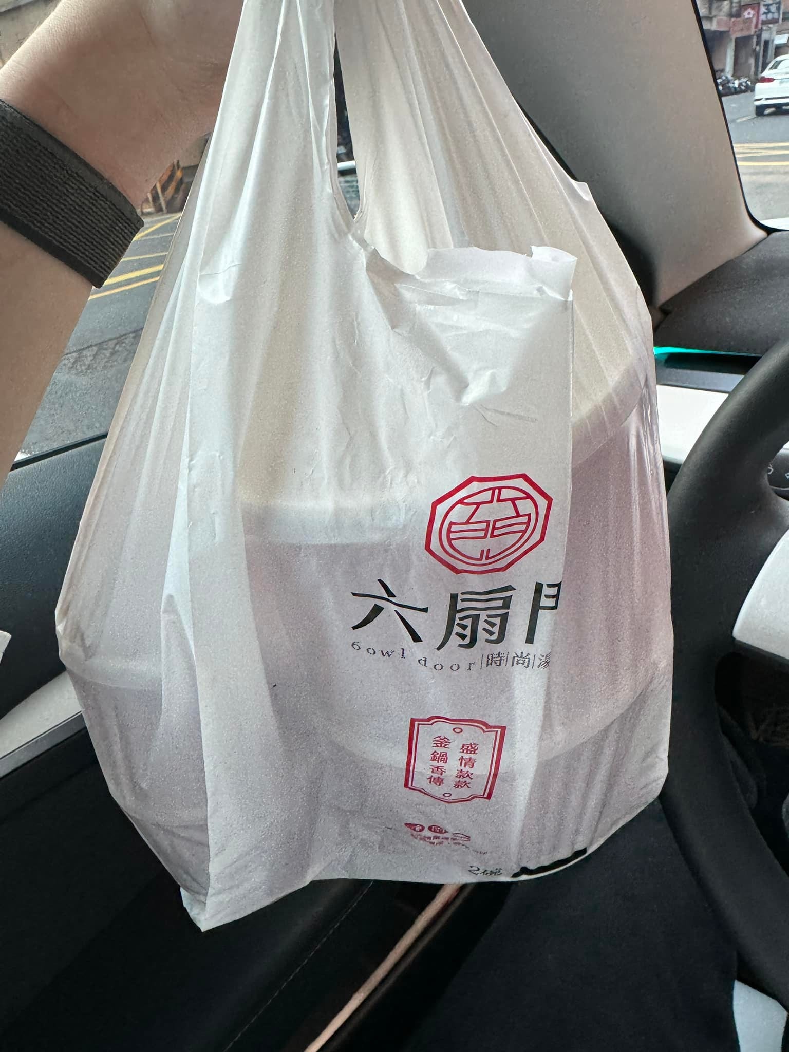 柯男在車內手提六扇門外帶袋，袋中是兩份火鍋