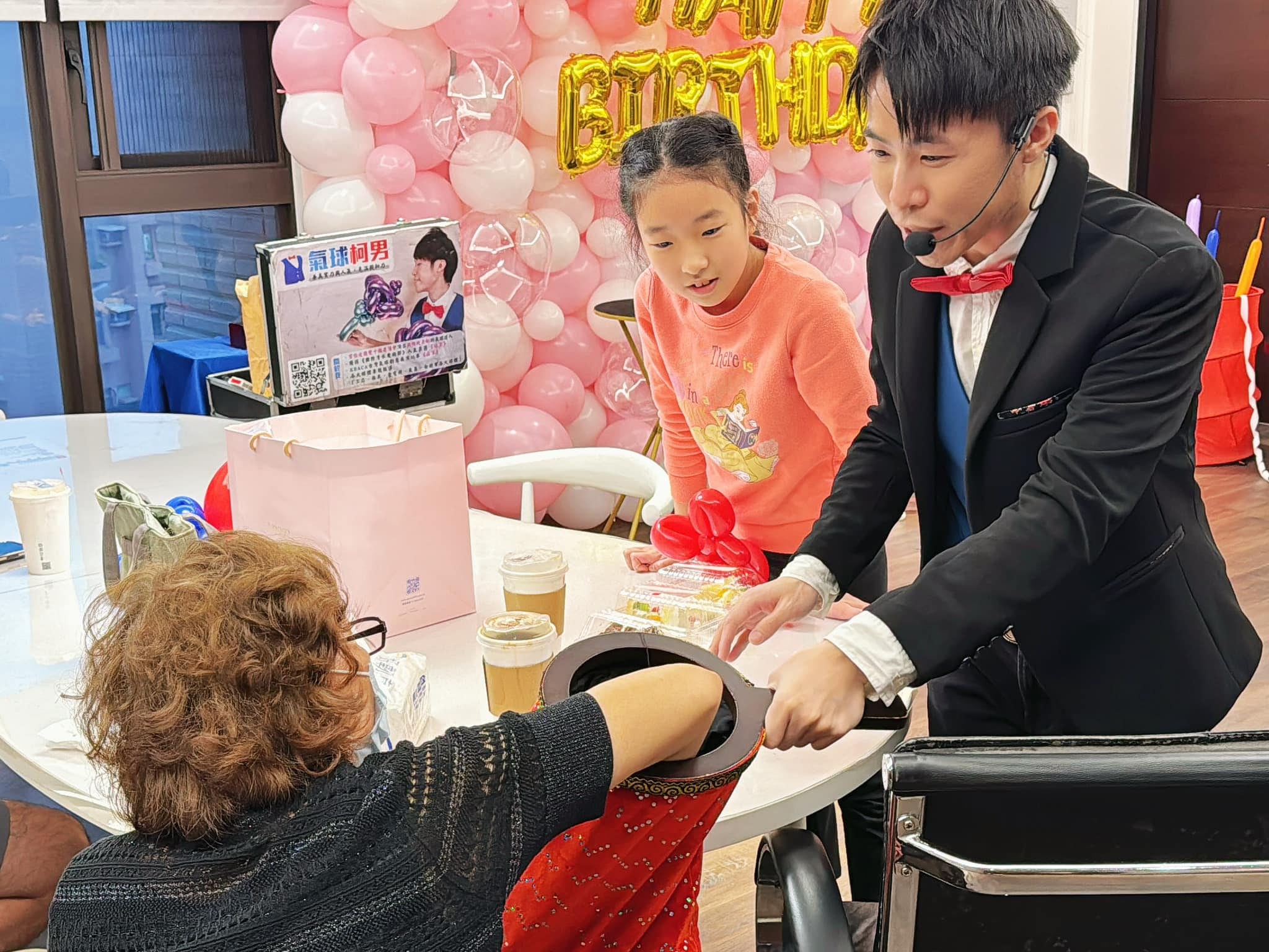 柯男在圓桌旁表演，長輩伸手配合魔術道具