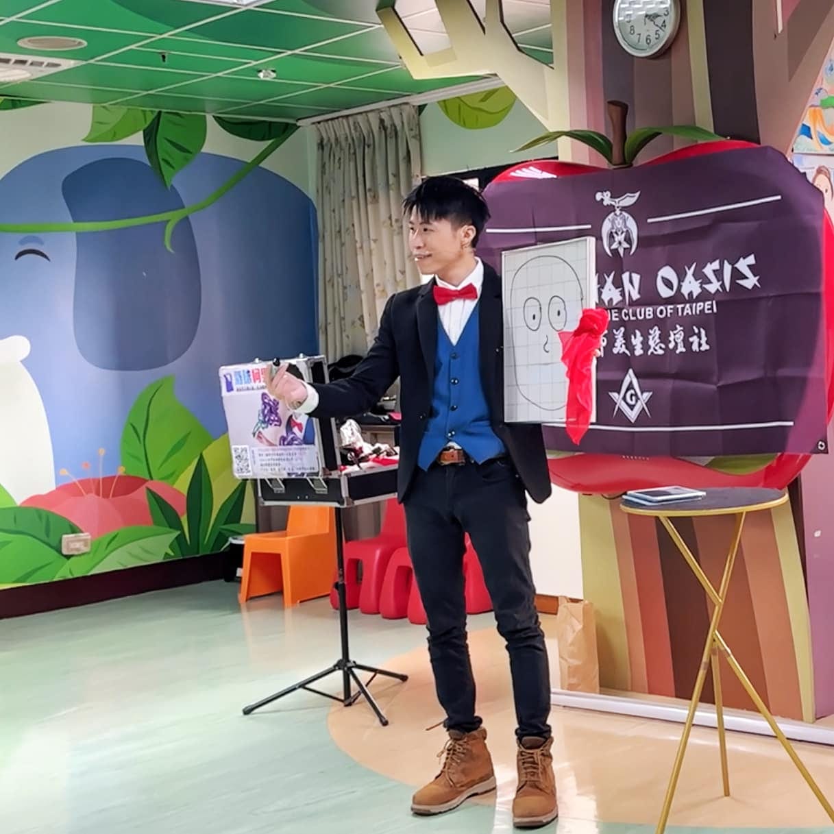 柯男在榮總兒童病房活動室表演魔術，旁邊掛著美生慈壇社旗幟