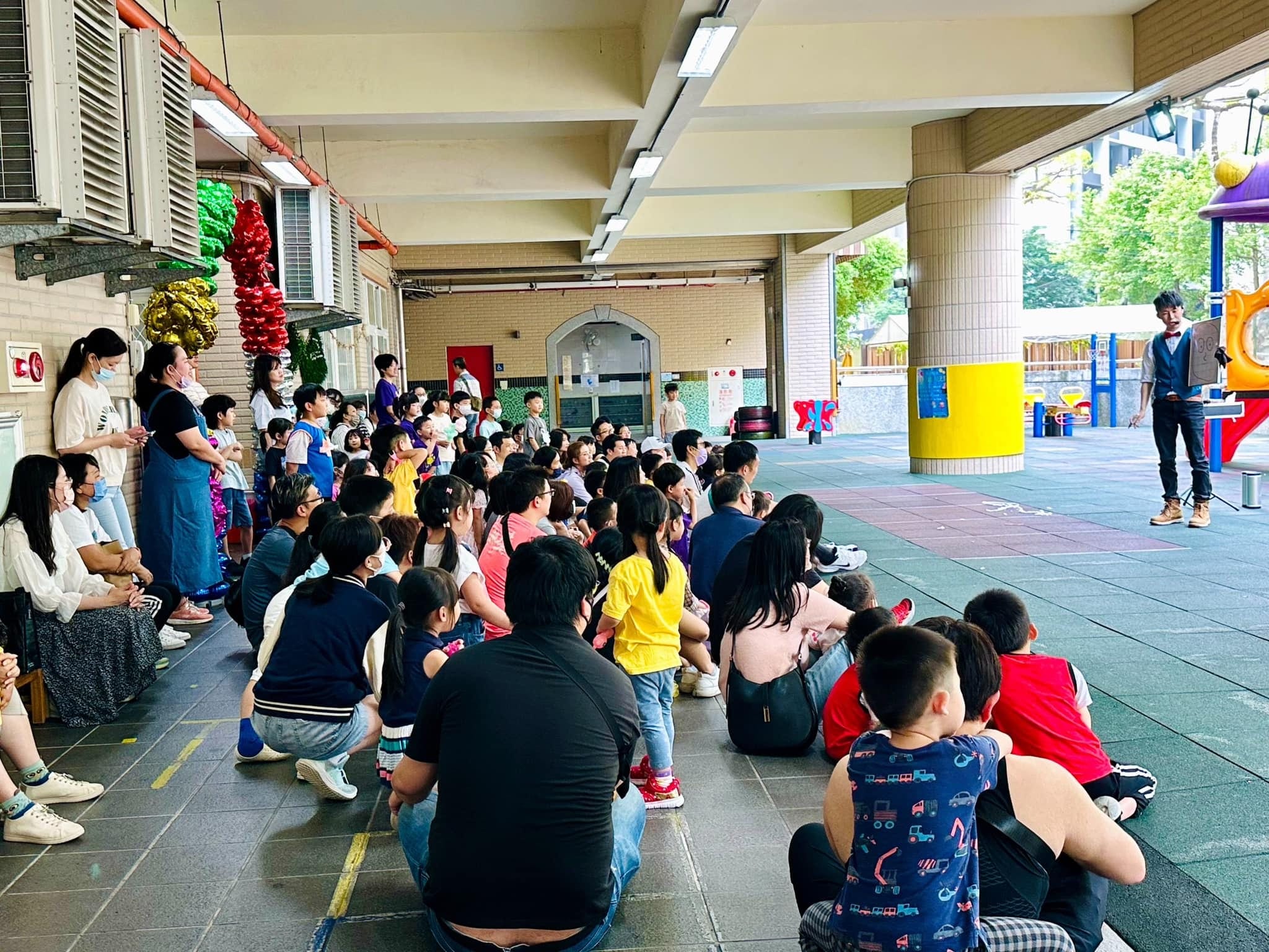 家長和孩子坐在走廊地上，看柯男在前方表演魔術