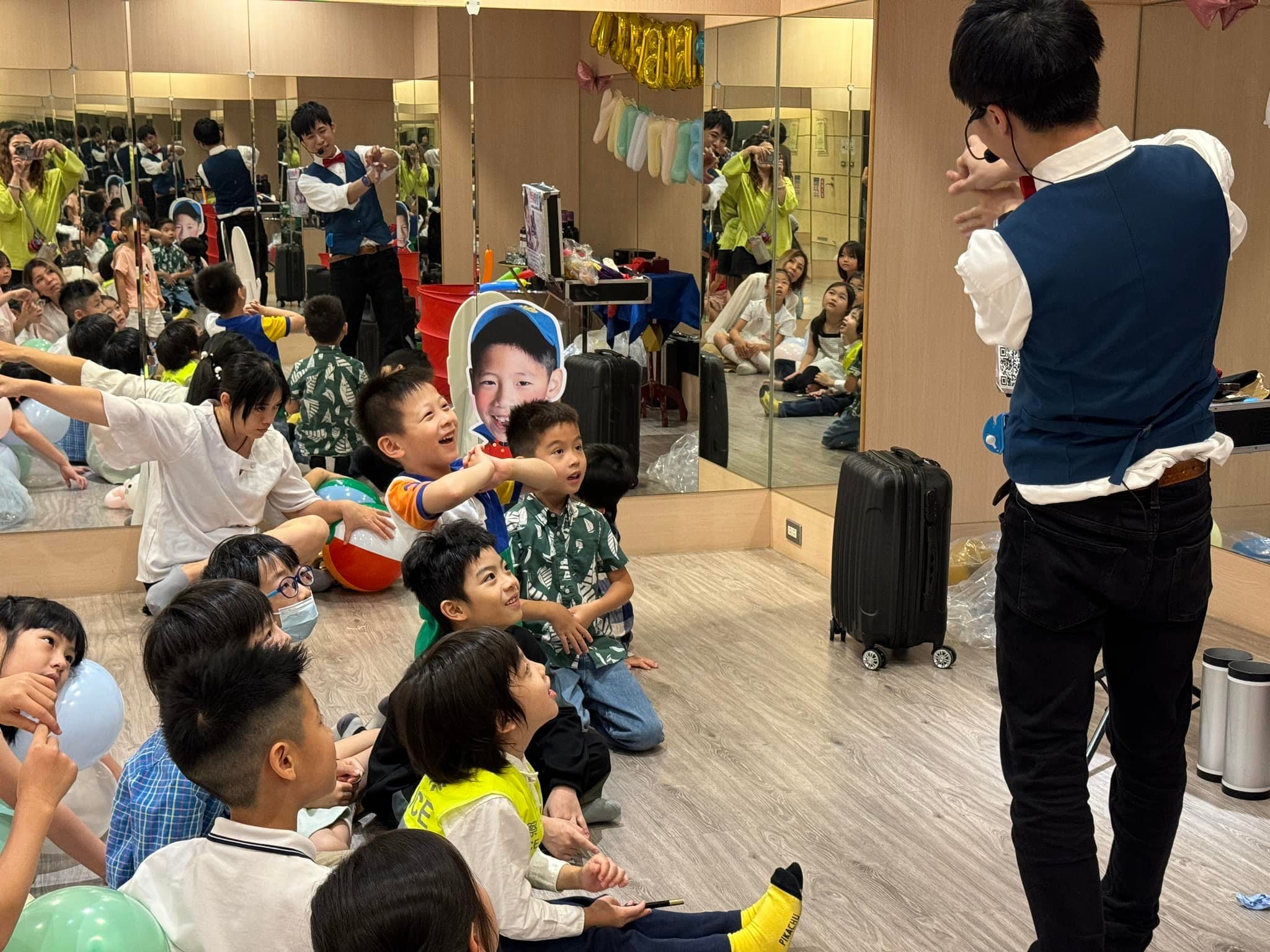 孩子們坐在木地板上，專心看柯男的魔術表演