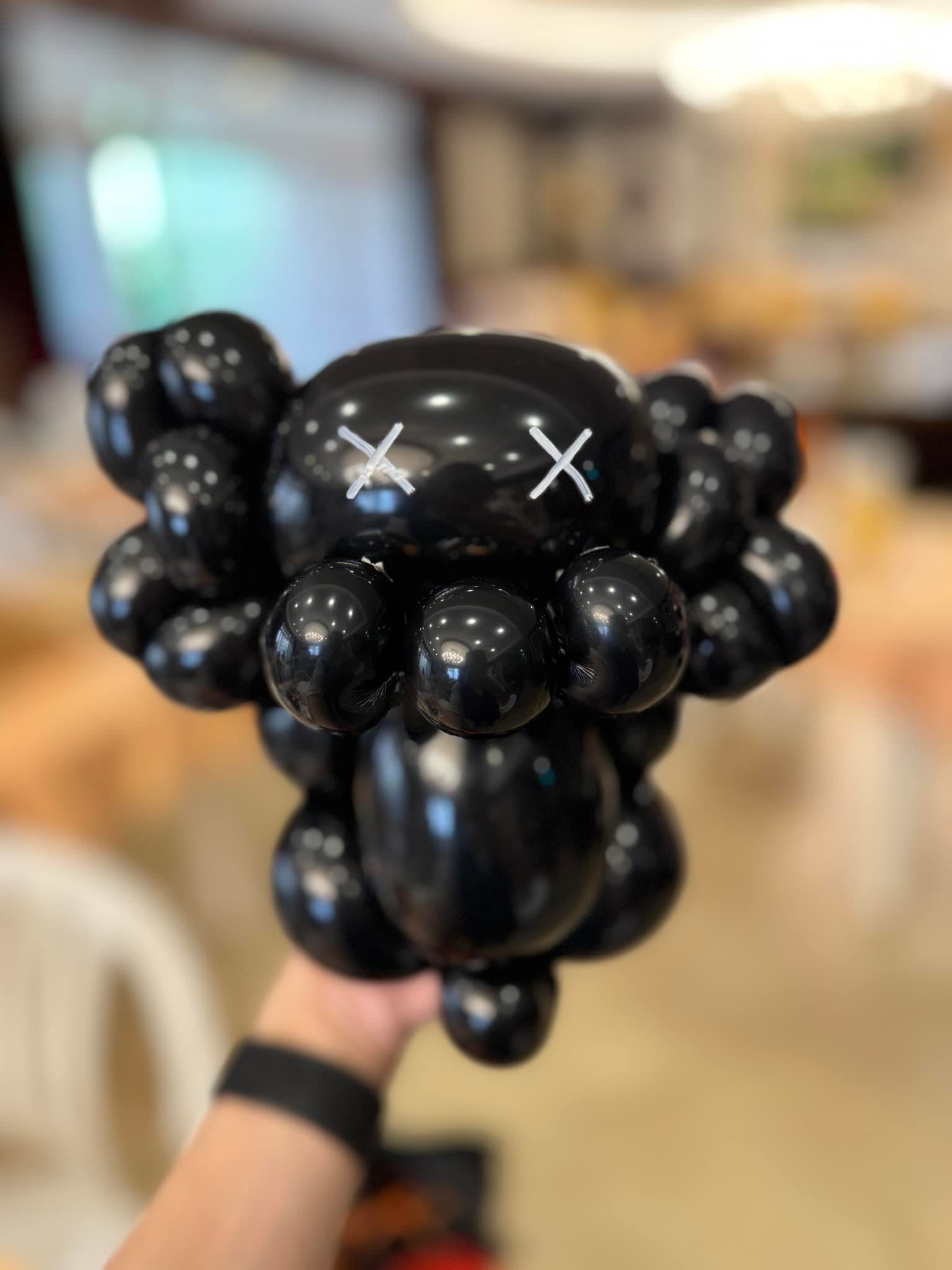 黑色 Kaws 公仔造型氣球近拍，臉上有兩個白色叉叉眼睛