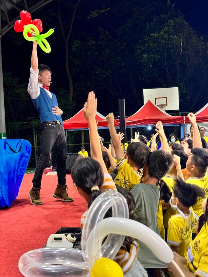 夜間戶外演出,柯男高舉造型氣球,穿黃色上衣的孩子們舉手互動