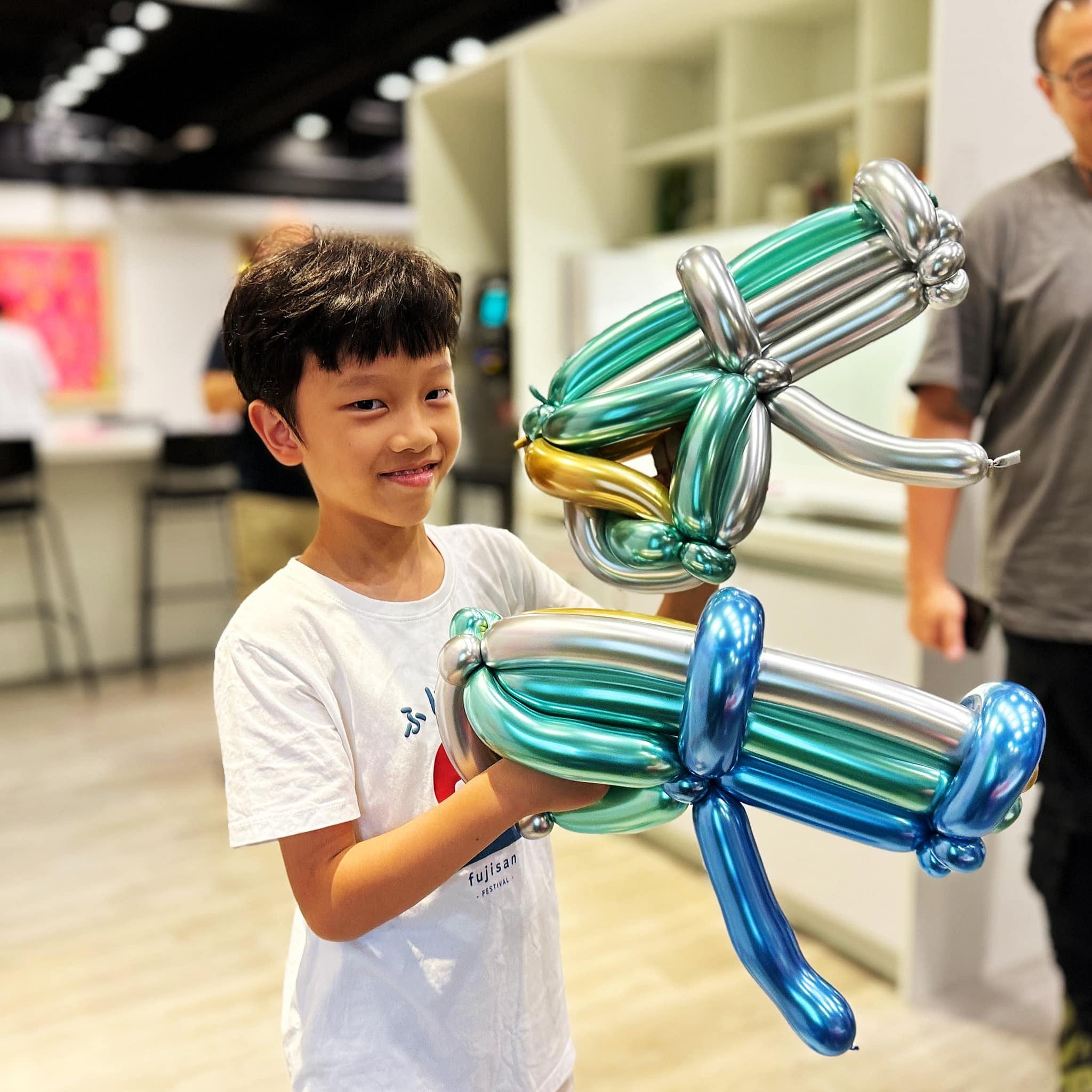 男孩抱著綠、銀、藍金屬色長氣球做成的武器造型