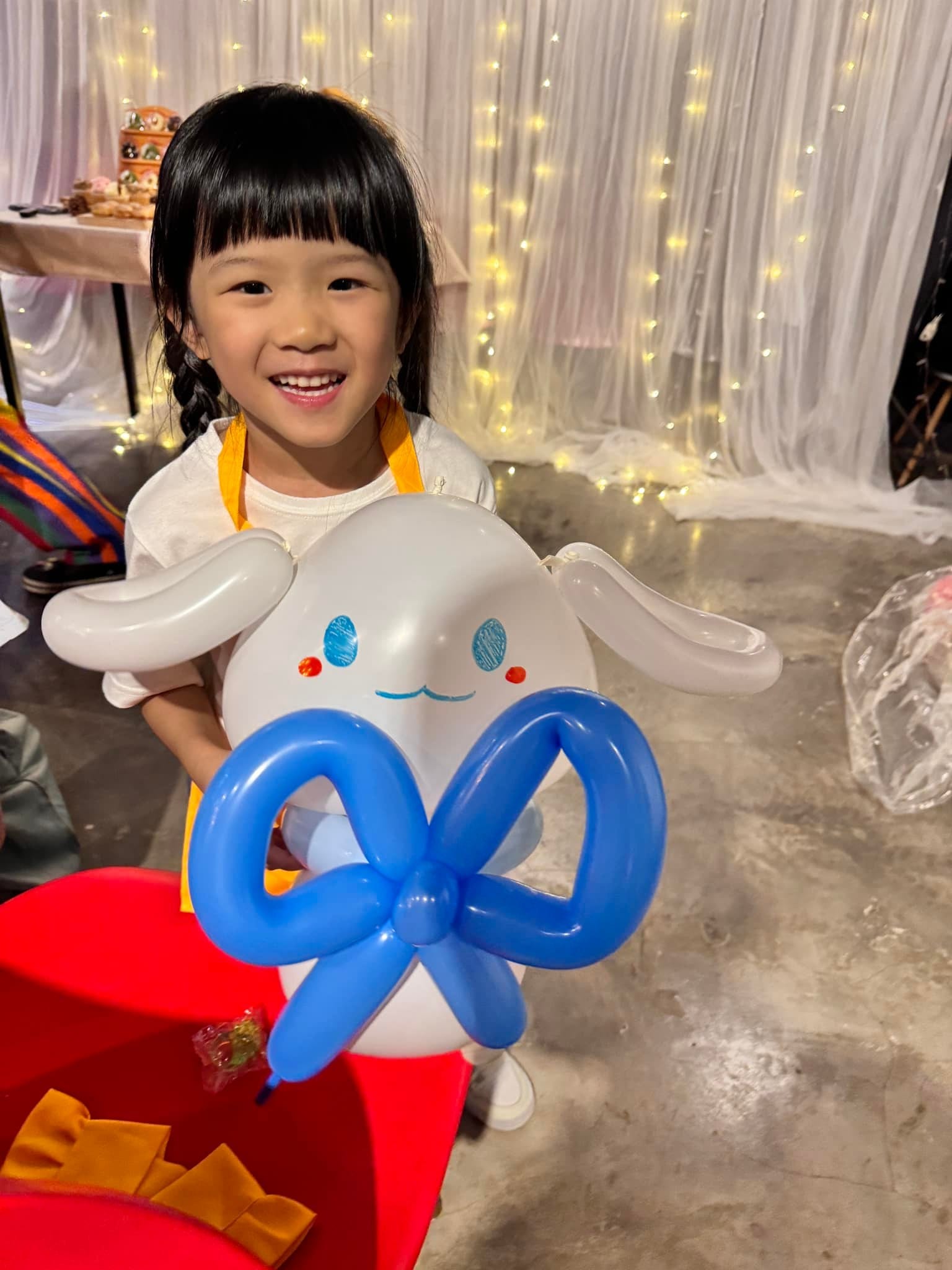 綁辮子的小女孩開心捧著藍色蝴蝶結的白色大耳狗造型氣球
