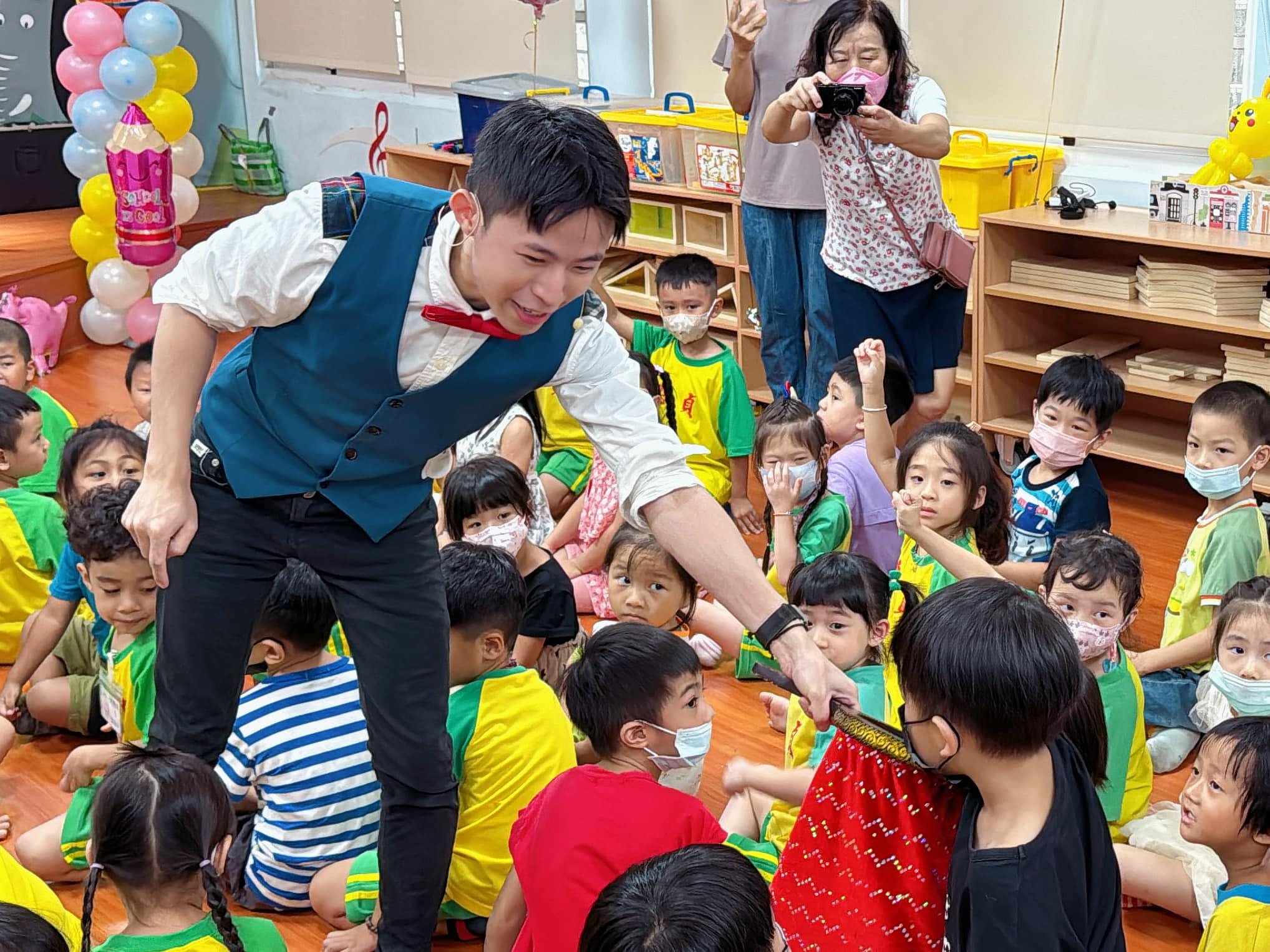 柯男拿著紅色魔術袋走到小朋友之間，請孩子伸手幫忙，家長在後方拍照