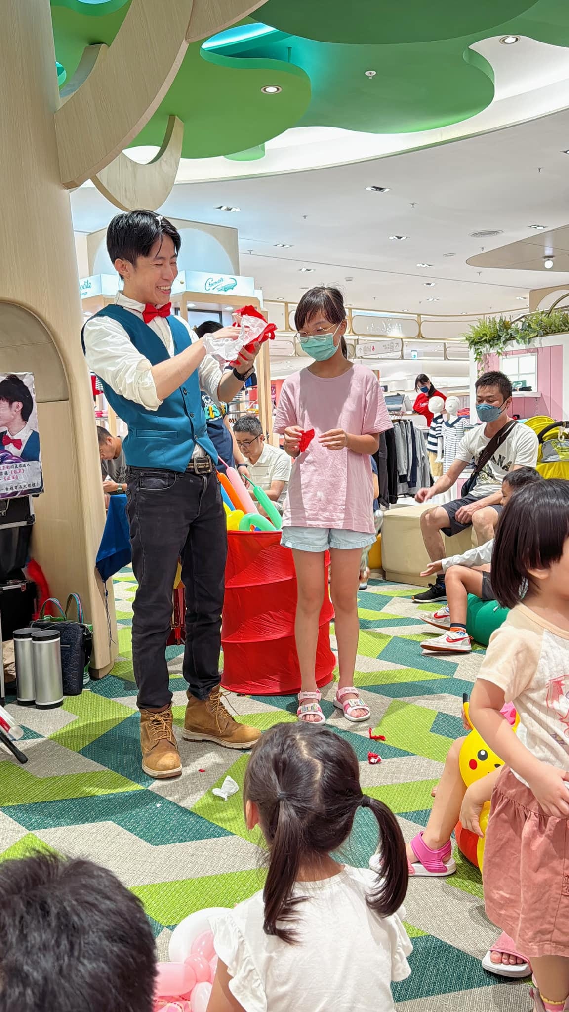 樹屋造型的綠色樹冠下，柯男邀請戴口罩的女孩上台一起表演魔術