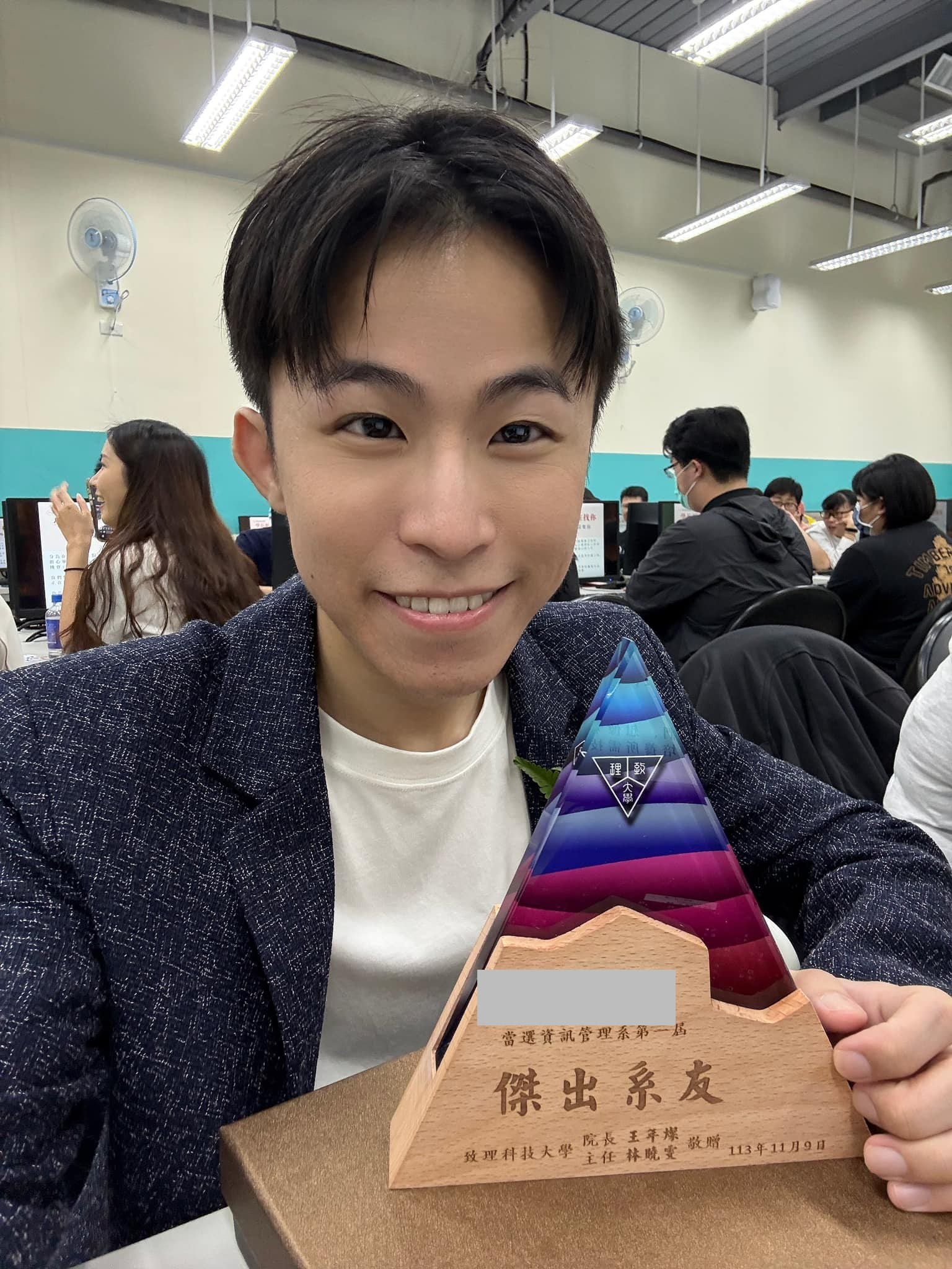 我拿著漸層三角造型的傑出系友獎座在教室裡自拍