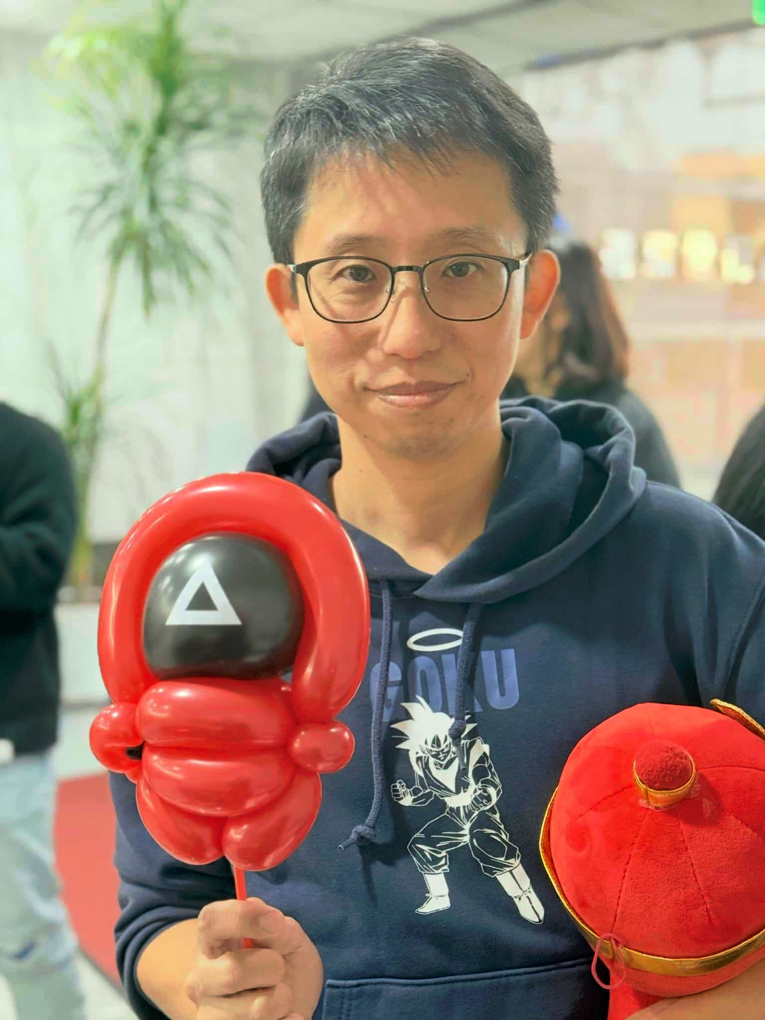 戴眼鏡的男士拿著紅色魷魚遊戲士兵造型氣球，黑色面罩上有白色三角形
