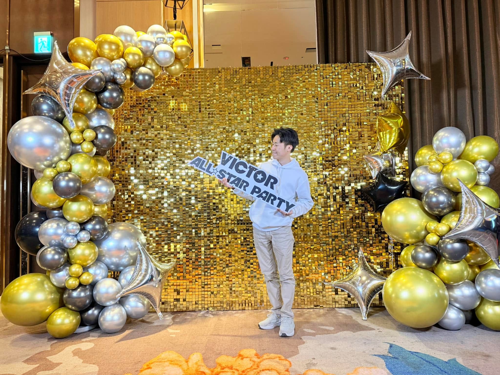 1 月亮片牆場：金色亮片牆兩側堆著金銀黑氣球，柯男拿派對手拿牌