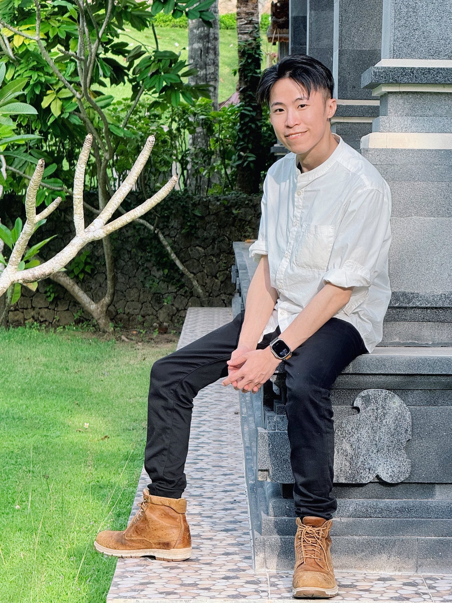 我穿白色立領襯衫坐在峇里島庭園的石座上