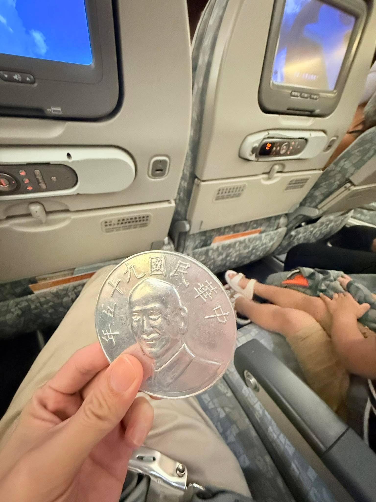 飛機座位上，我手裡拿著一枚比一般大很多的巨大硬幣
