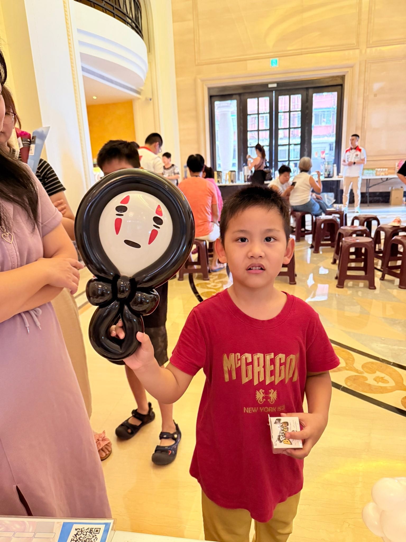 大廳折氣球那場：男孩舉著無臉男造型氣球