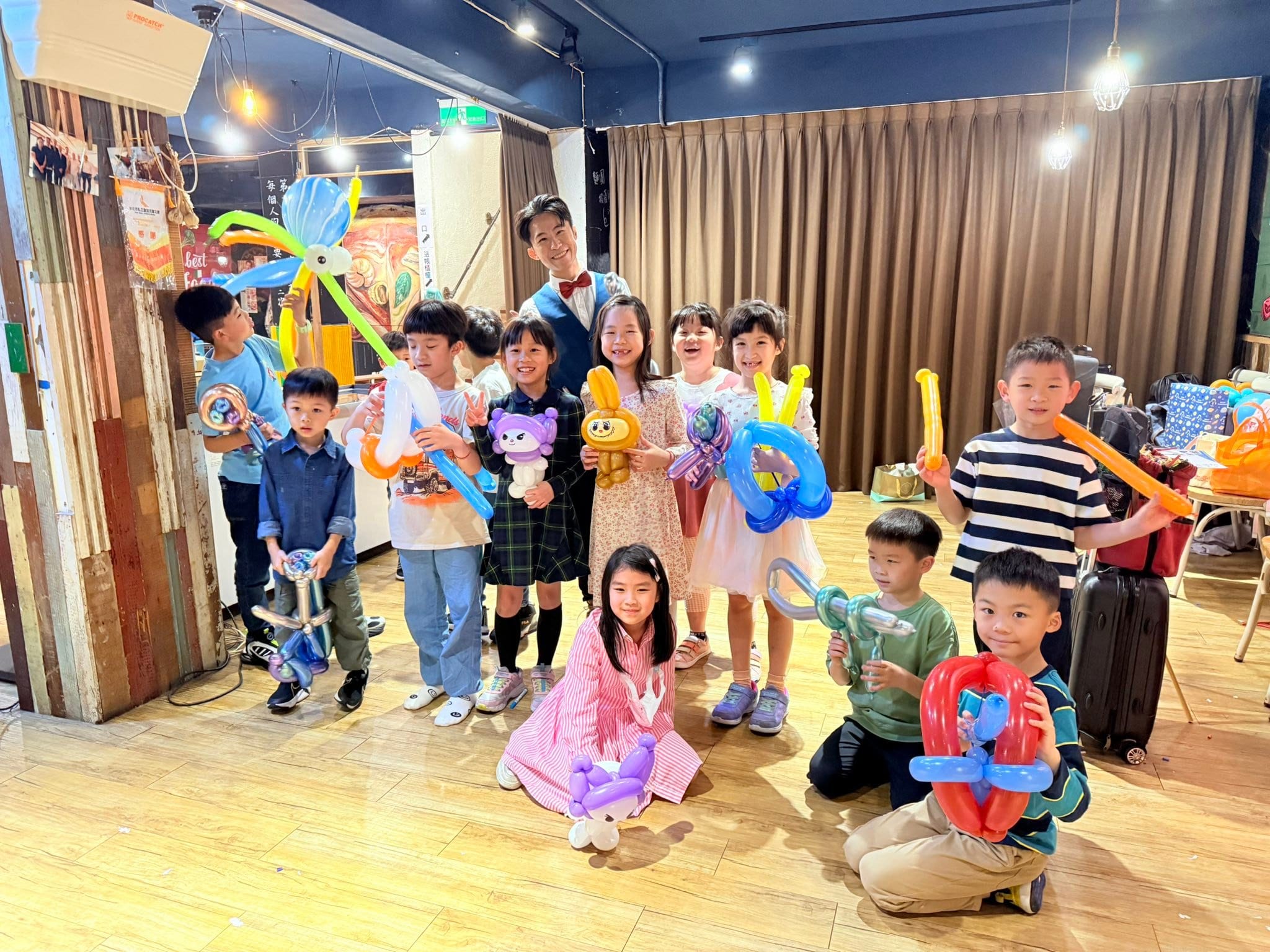 披薩餐廳裡，小朋友拿著章魚、寶劍、金色兔耳娃娃和愛心造型氣球和柯男合照
