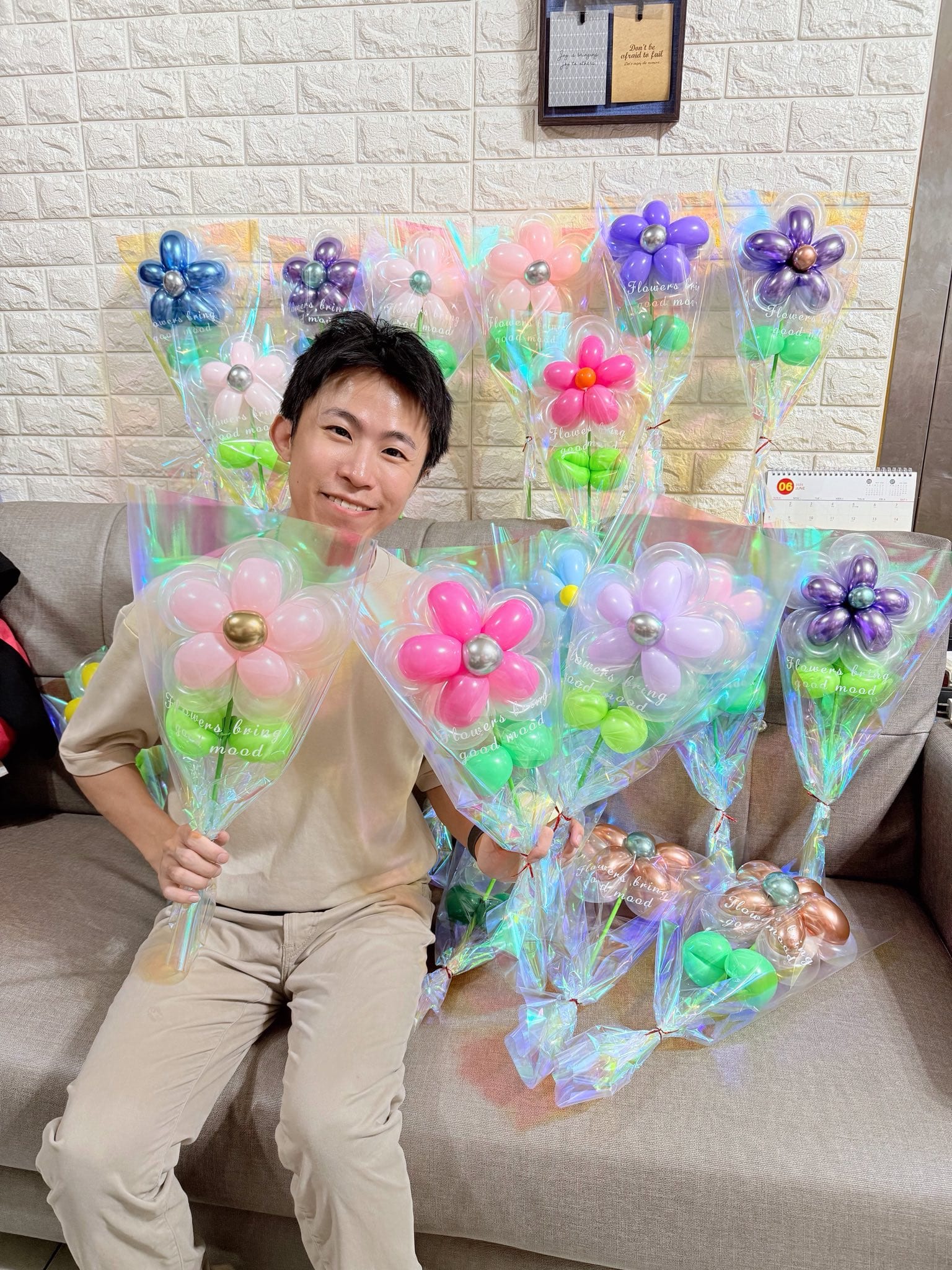 柯男坐在沙發上，手拿粉色與桃紅色的鐳射包裝氣球花，身後排滿其他顏色的氣球花