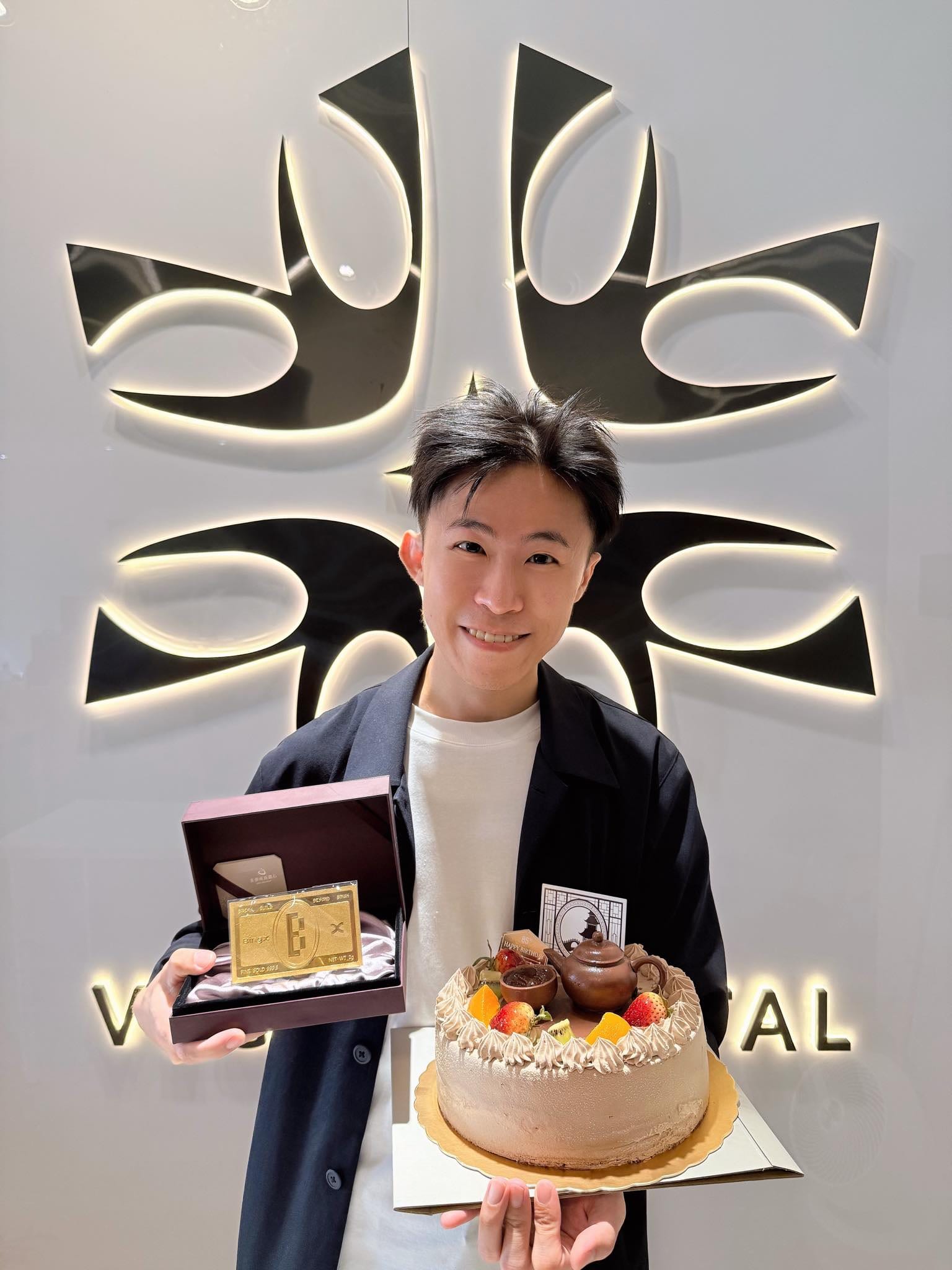 我一手拿生日蛋糕、一手拿金色禮盒，站在發光的牆面前