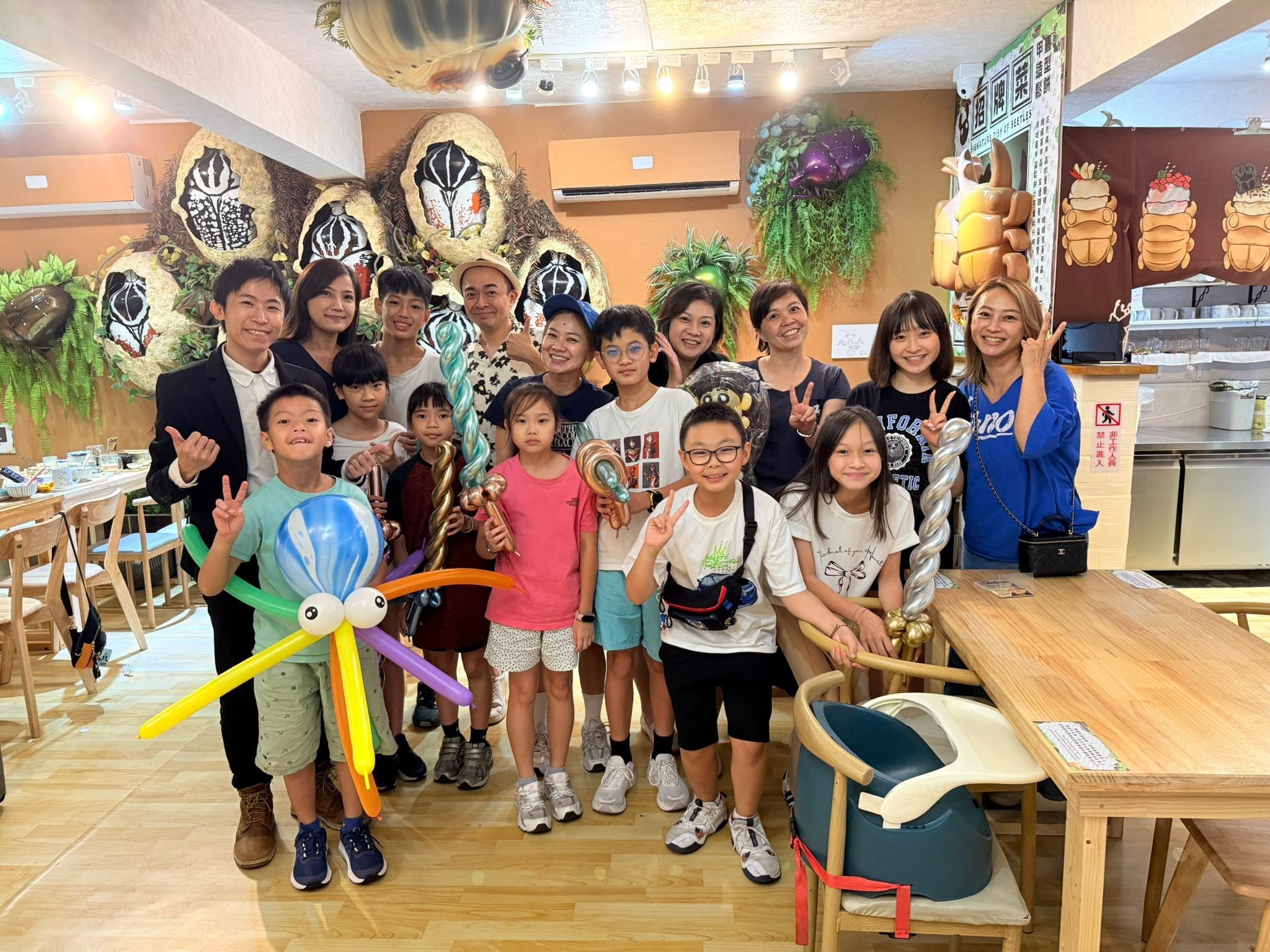 生日派對魔術表演後在餐廳大合照，穿綠衣的壽星拿著彩虹章魚氣球，其他小朋友拿著金屬色寶劍