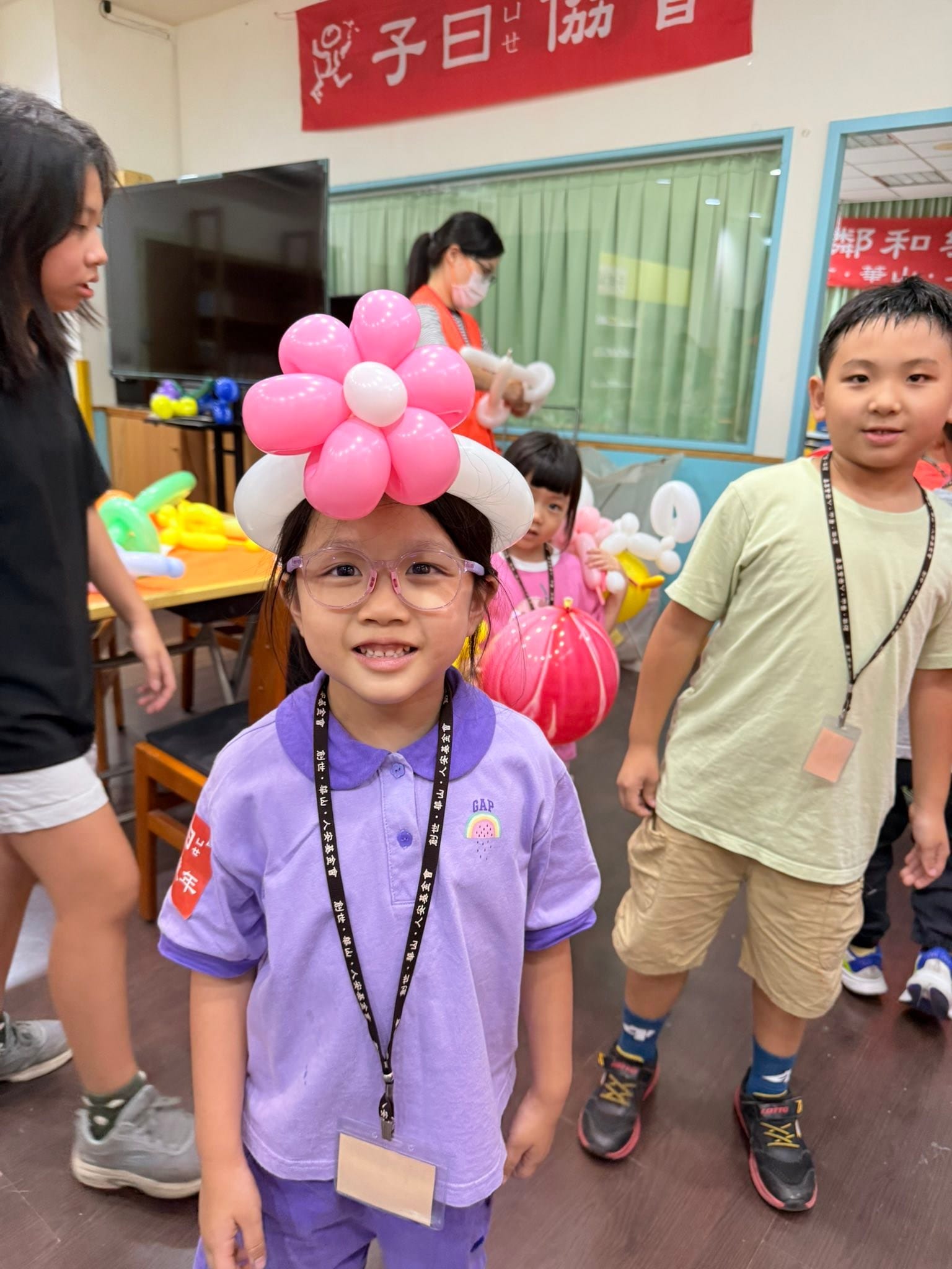 戴眼鏡的小女孩頭上戴著粉紅色花朵、白色帽圈的氣球帽子