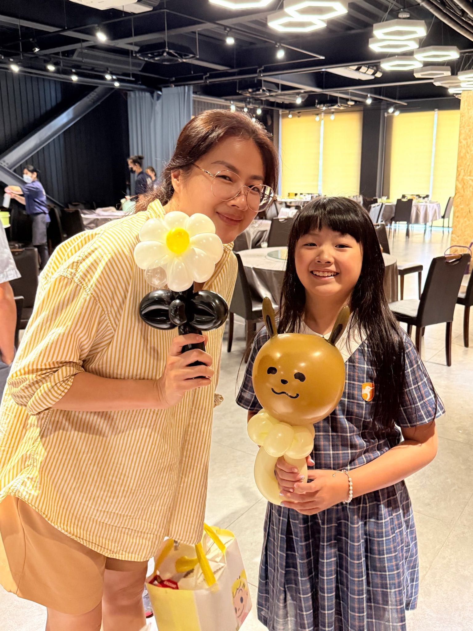 媽媽拿著白色小雛菊氣球，女兒捧著咖啡色伊布造型氣球棒