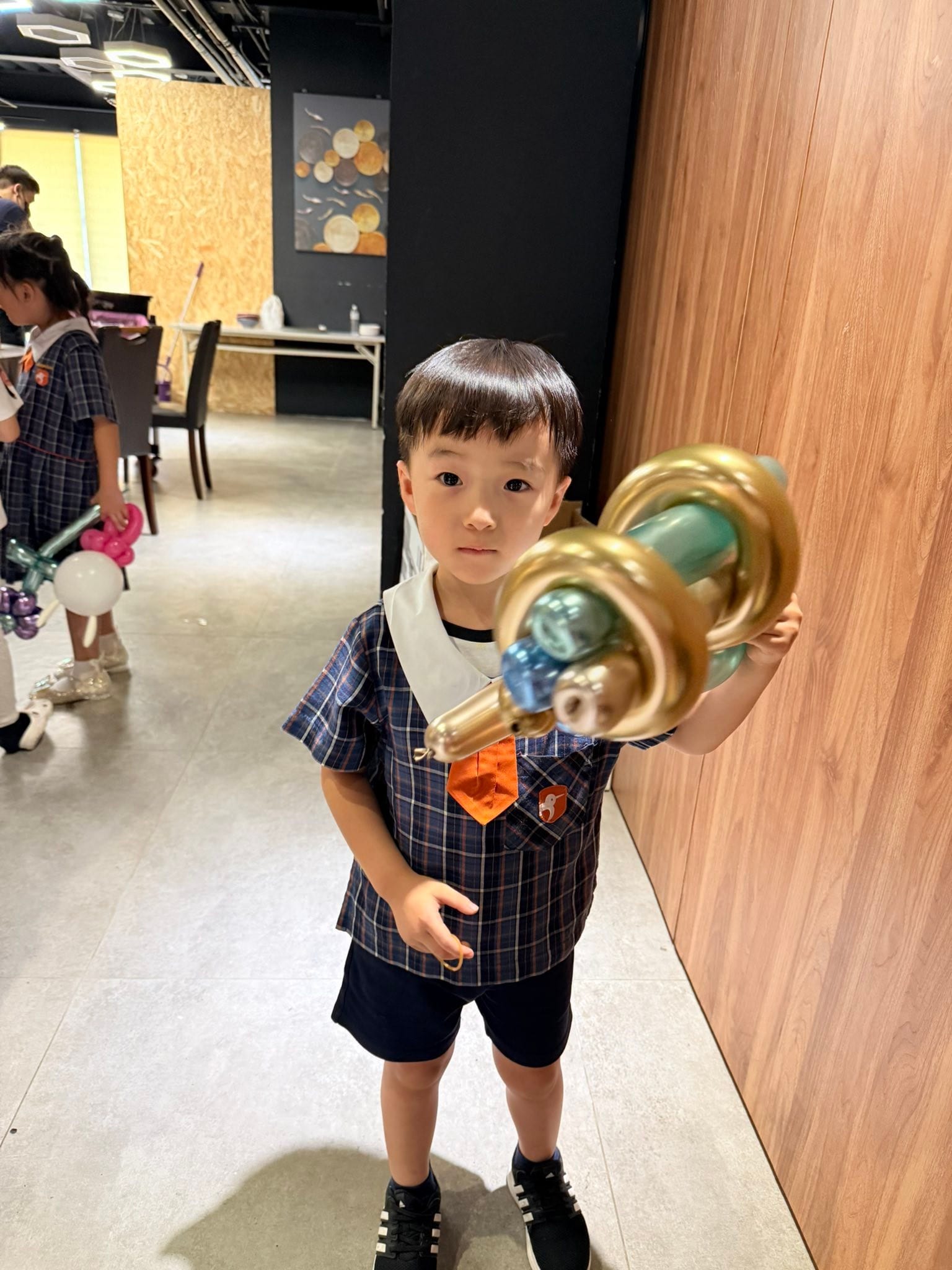 穿格子制服的小男孩舉著金色與藍綠色金屬氣球做的雷射大槍