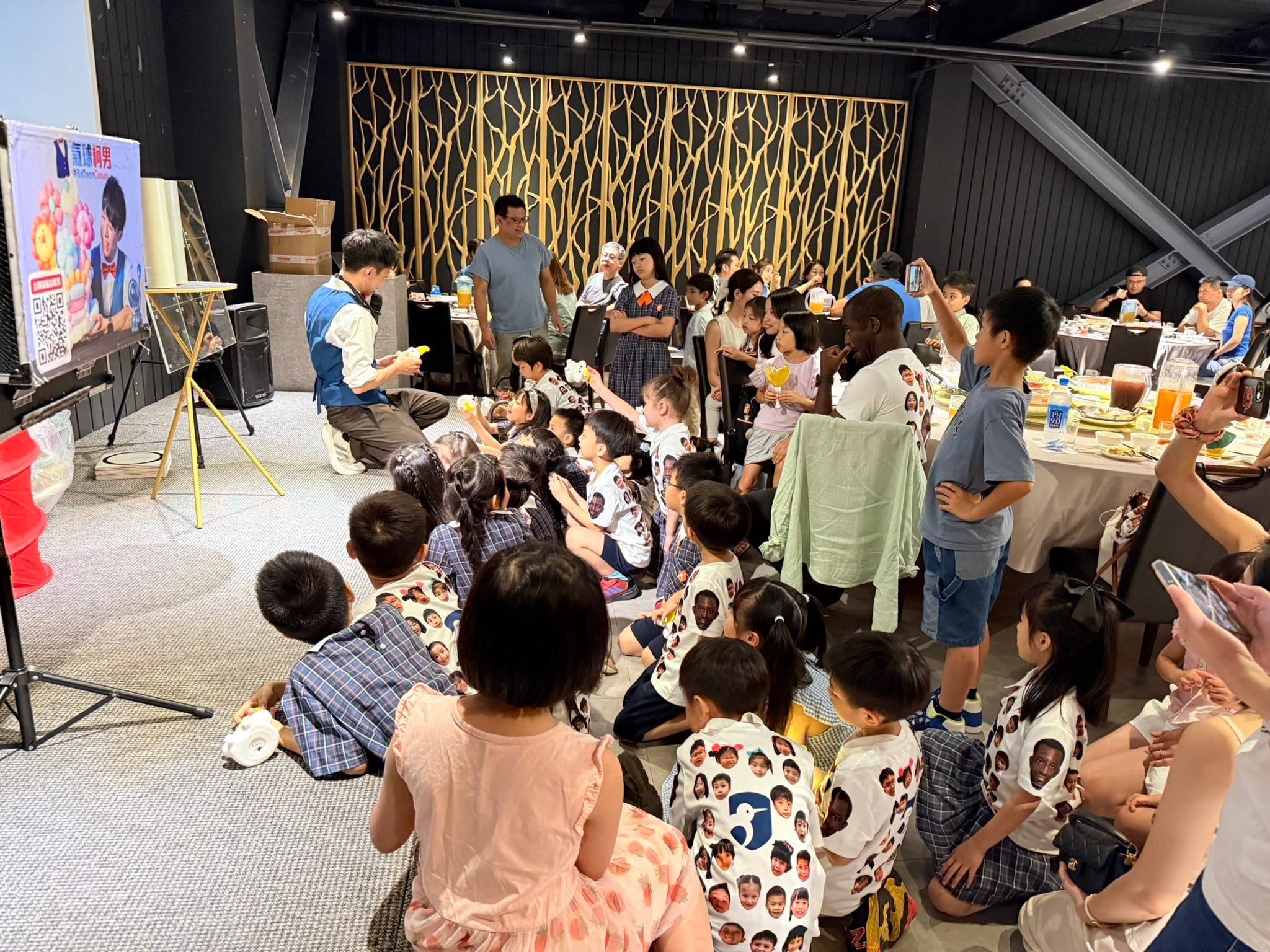 謝師宴兒童魔術表演，穿格子制服和班服的小朋友坐在地毯上圍著柯男看表演