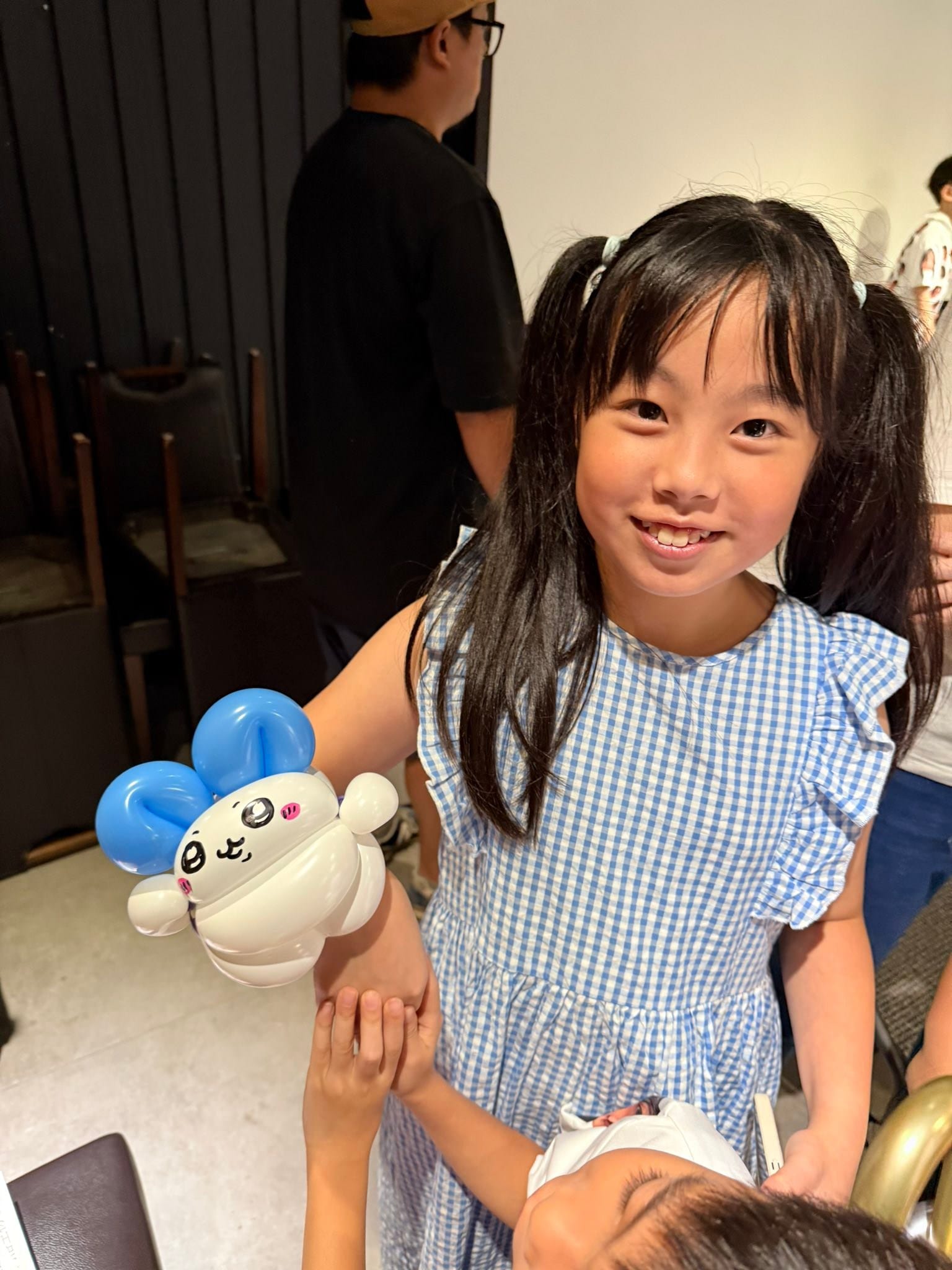 穿藍白格子洋裝的女孩拿著白色身體、藍色圓耳朵的吉伊卡哇「小八」造型氣球手環