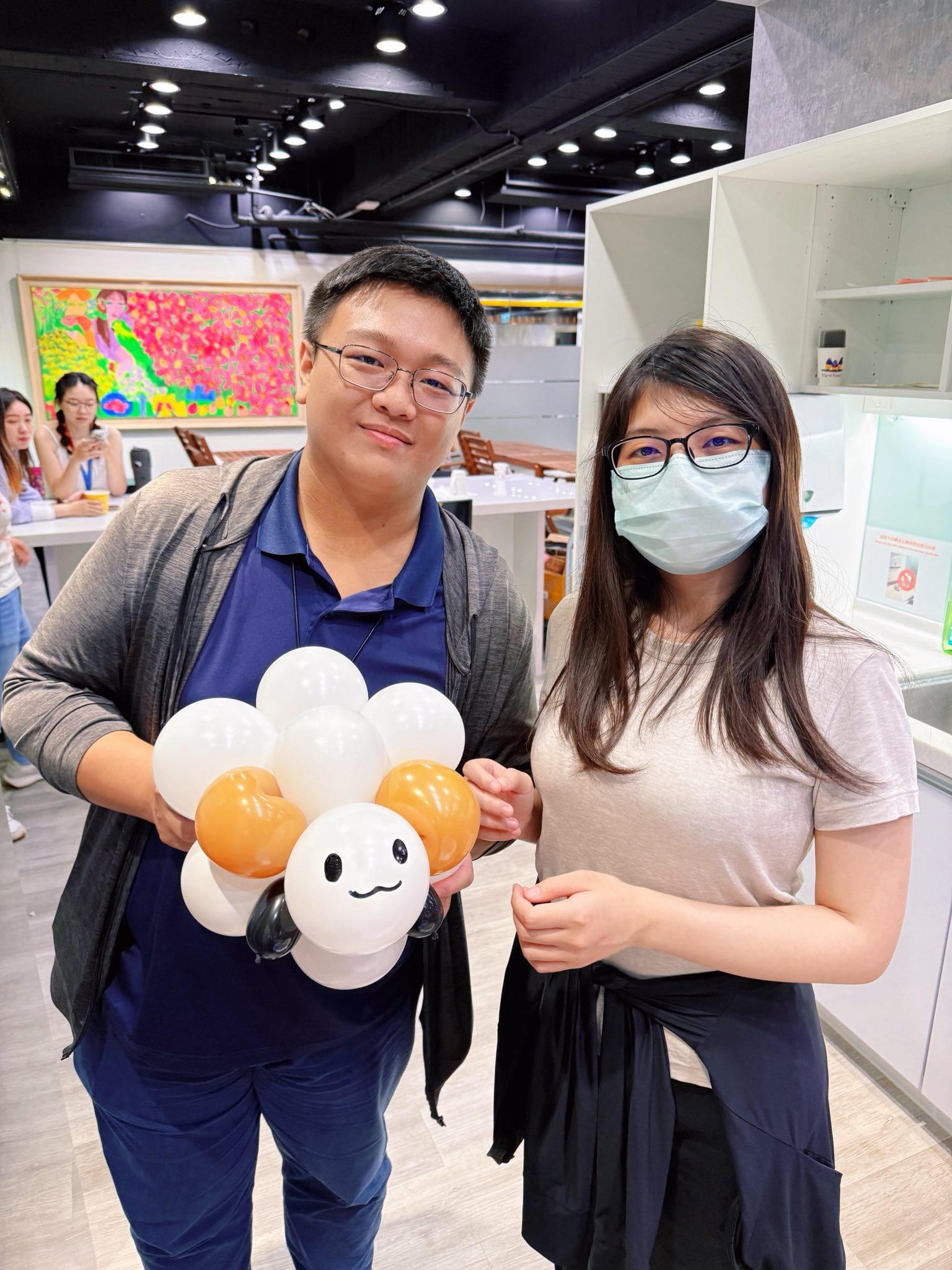 兩位員工合照，其中一位抱著白色捲毛、橘色耳朵的綿羊造型氣球