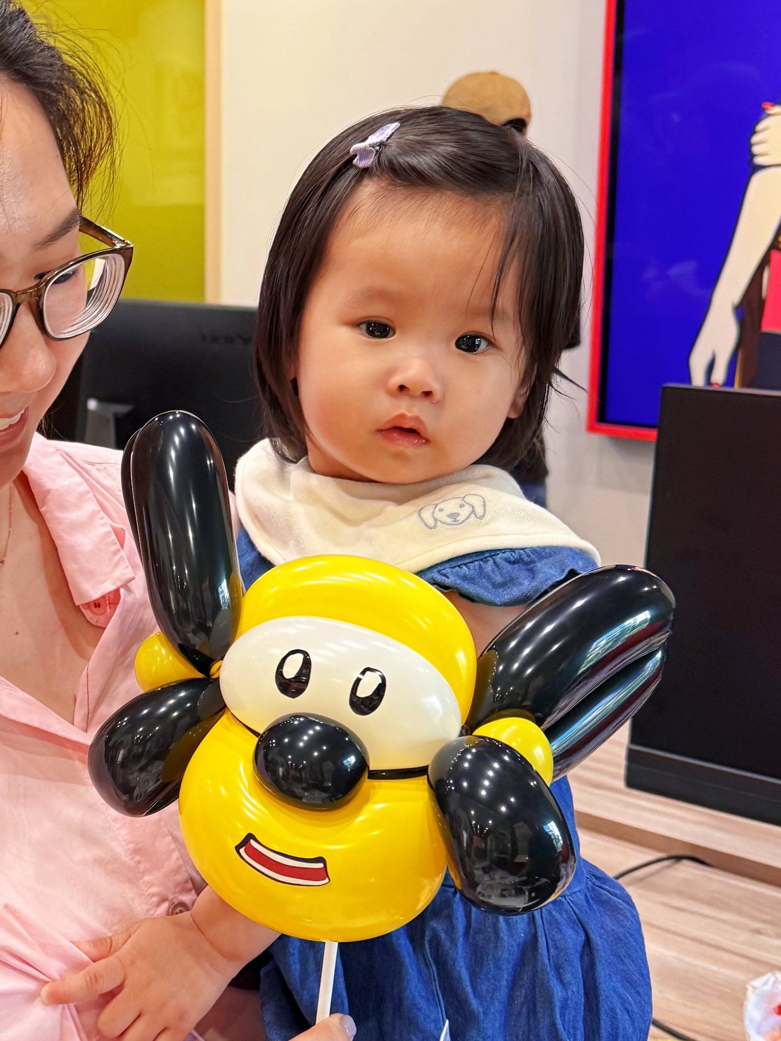 媽媽抱著幼兒，幼兒手上拿著黃色臉、黑色大耳朵的小狗造型氣球