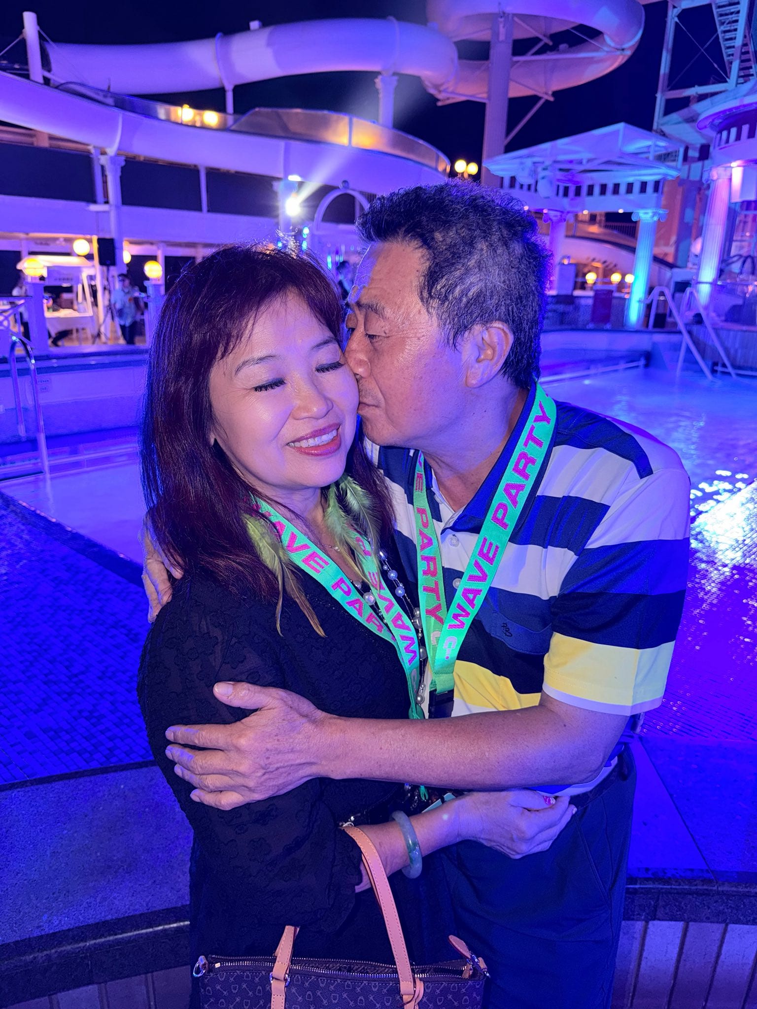 爸爸在郵輪泳池甲板的夜晚親吻媽媽的臉頰