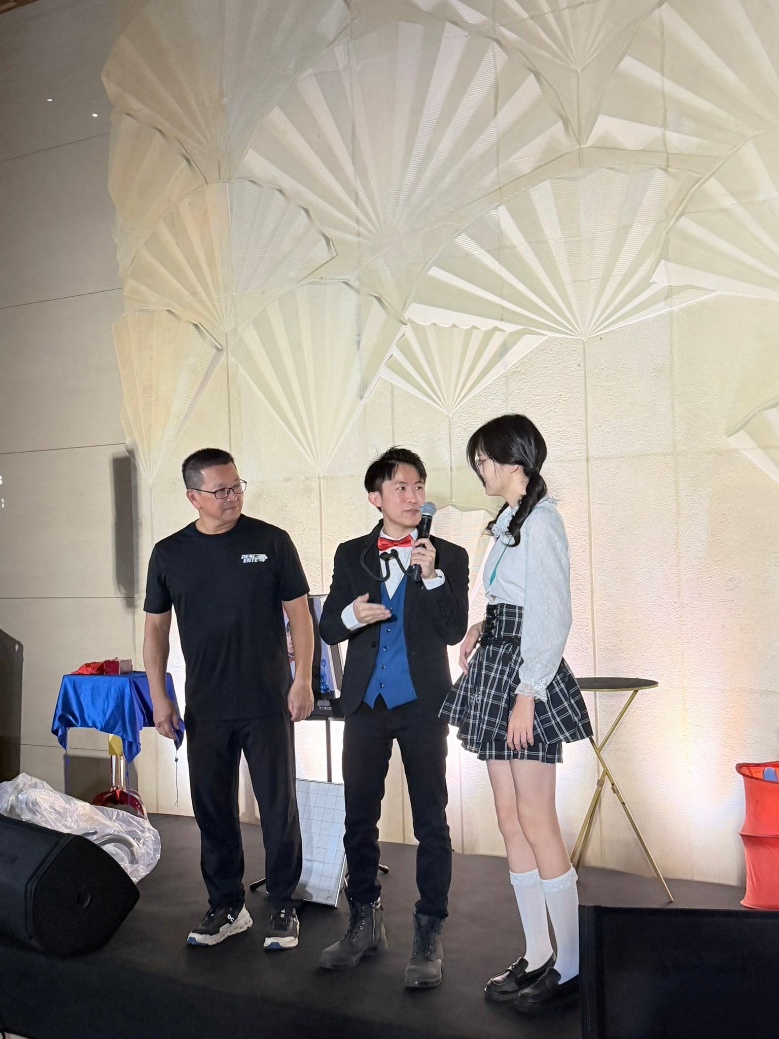 柯男拿著麥克風站在舞台中間，左邊是穿黑色上衣的男性住戶，右邊是穿制服裙的女生
