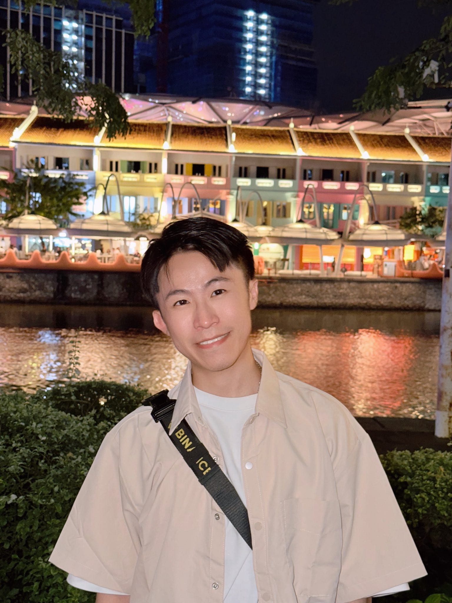 我站在新加坡河岸邊，背後是夜晚燈火通明的彩色店屋