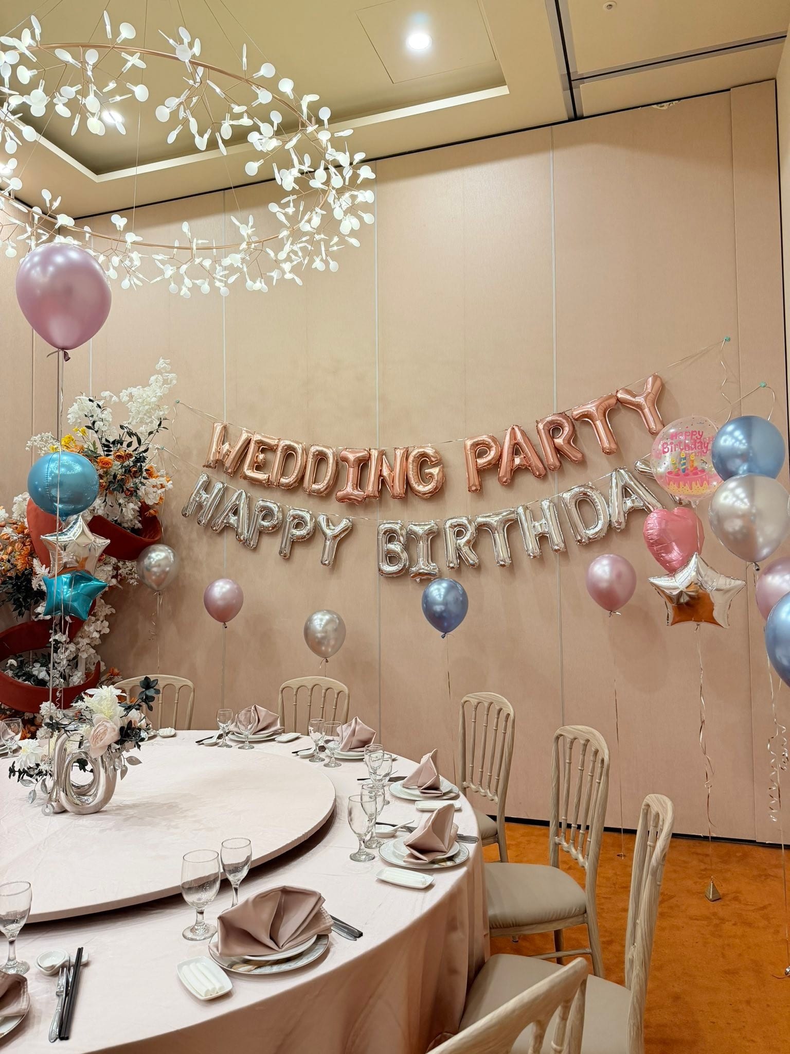 包廂牆上掛著玫瑰金 WEDDING PARTY 與銀色 HAPPY BIRTHDAY 字母氣球，旁邊點綴粉、藍、銀色氣球
