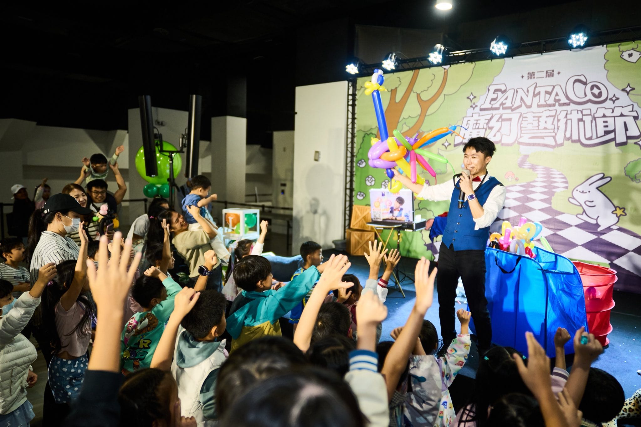 柯男在 FANTACO 舞台上舉著彩色造型氣球,台下孩子們舉手歡呼
