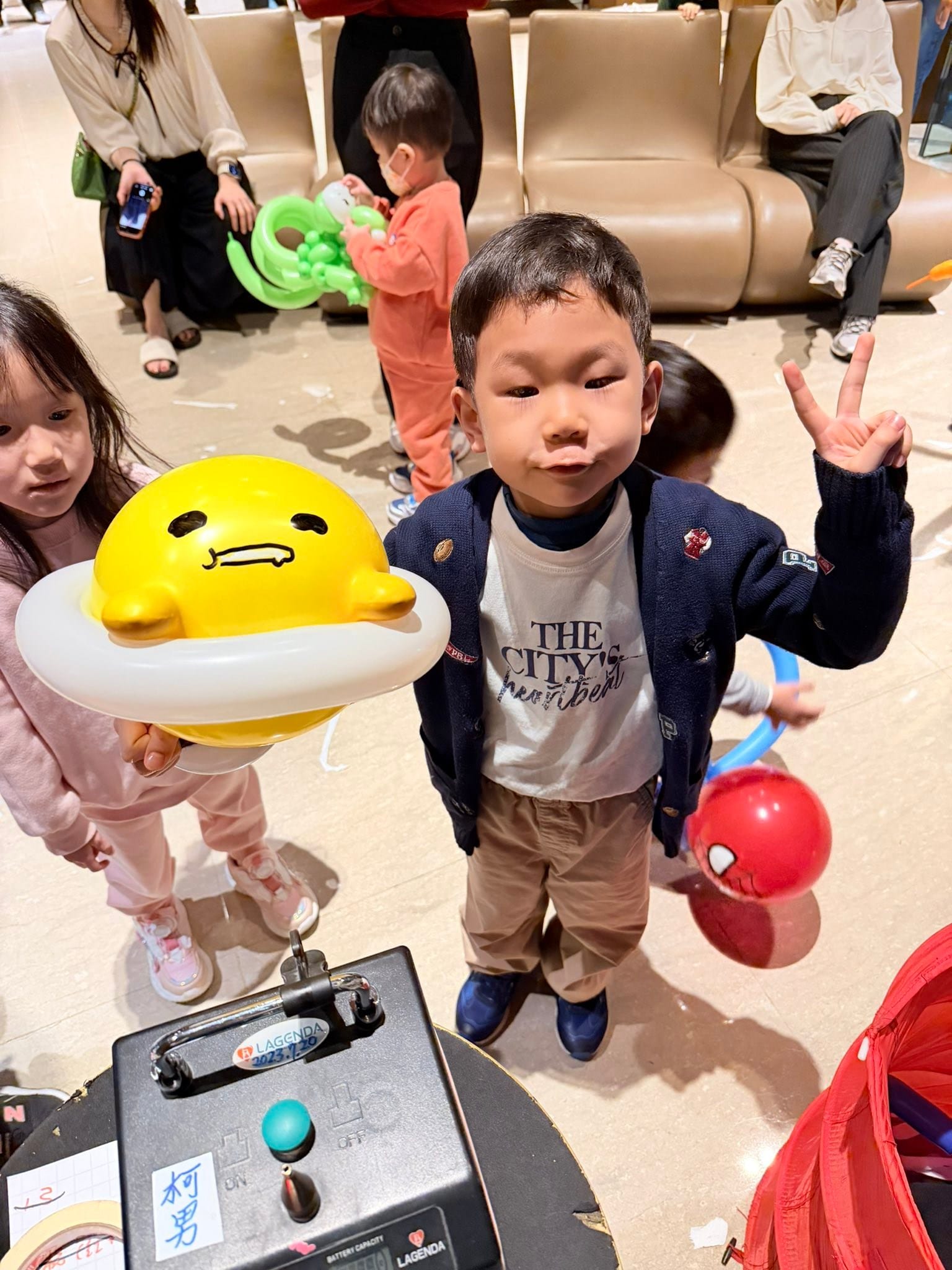 1 月生日派對：小男孩比 YA，女孩拿著黃色蛋黃造型氣球
