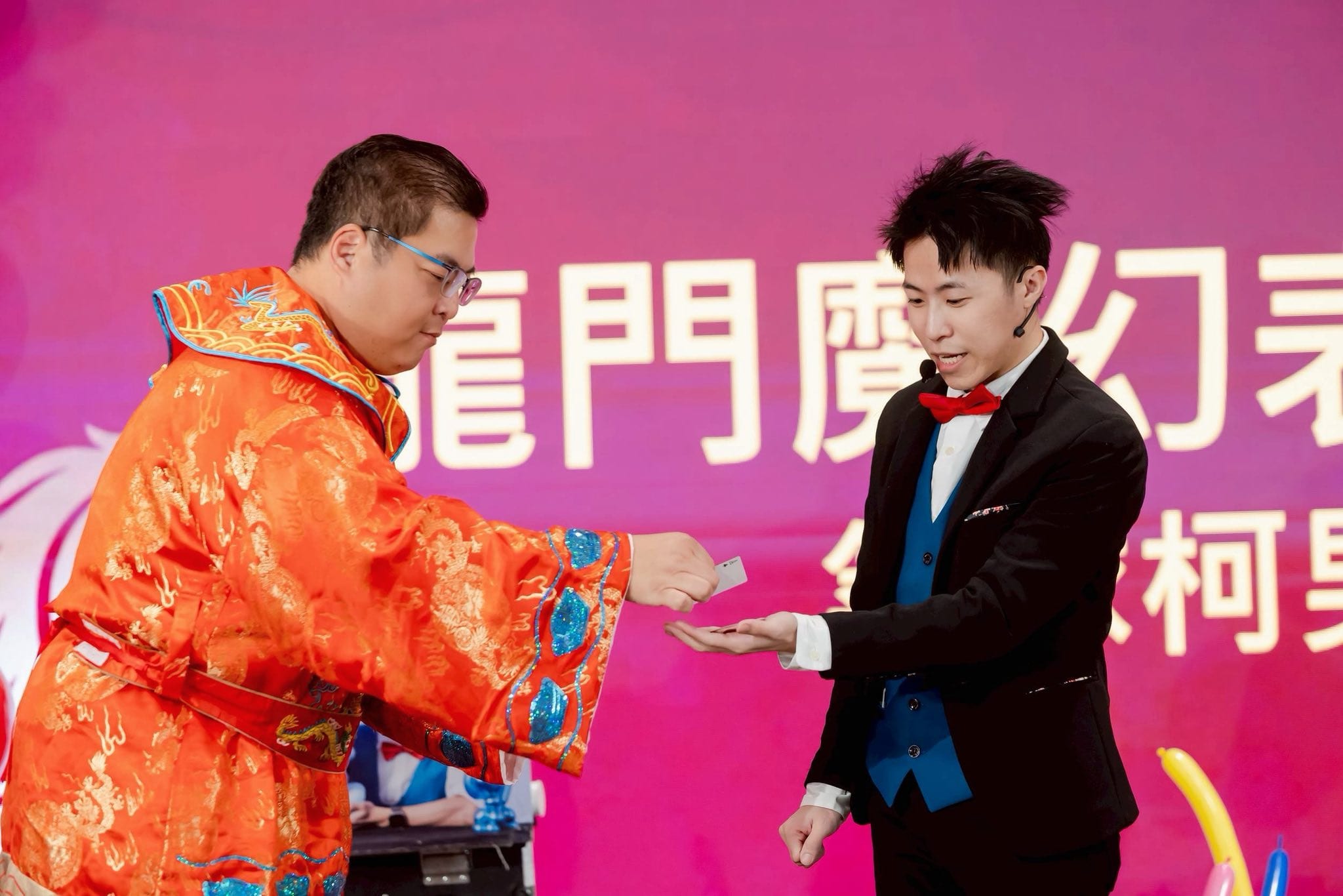 穿橘色古裝的來賓把一張卡片遞到柯男手上，背景是龍門魔幻表演秀字樣