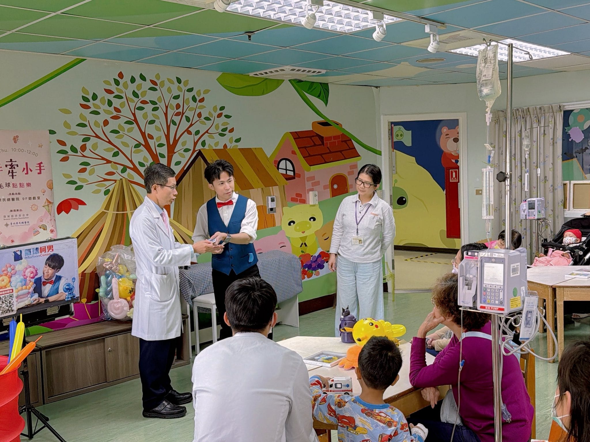 病房遊戲室彩繪牆前，穿白袍的醫師與柯男站在台前開場，孩子們坐在桌邊觀看