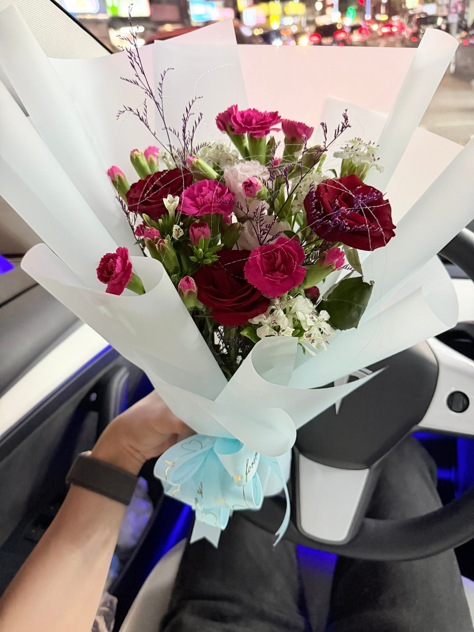 車上拿著紅玫瑰、粉色小花與淺藍包裝的真花花束