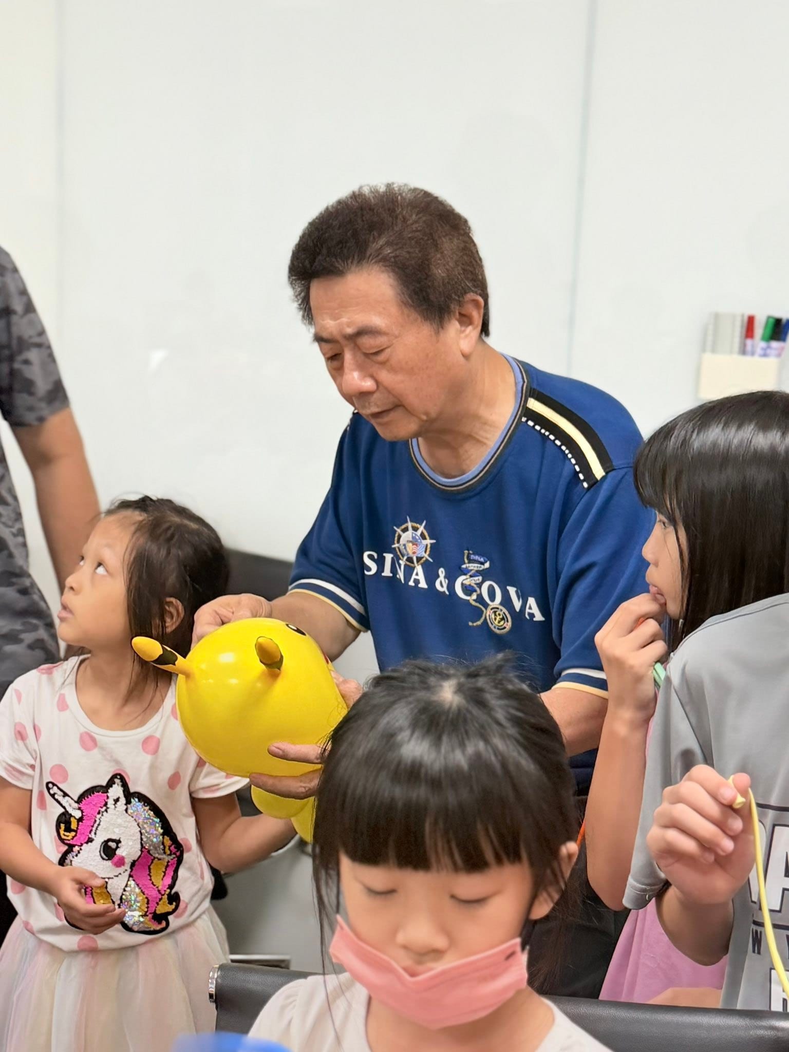 穿深藍色上衣的男士在會議桌旁協助小女孩調整黃色氣球的耳朵造型
