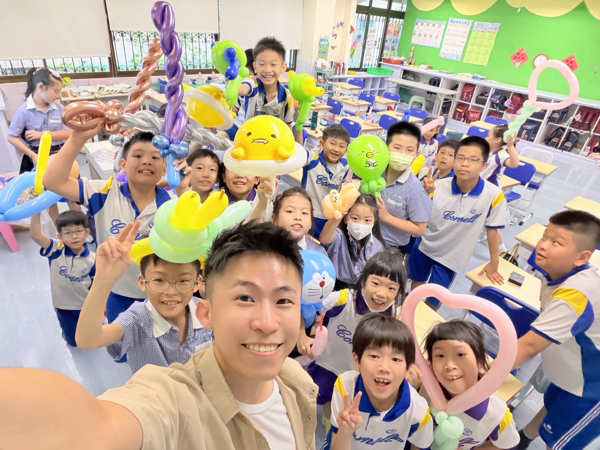 柯男在教室裡自拍，身後的國小學生高舉黃色蛋黃造型、愛心、寶劍等期末禮物氣球