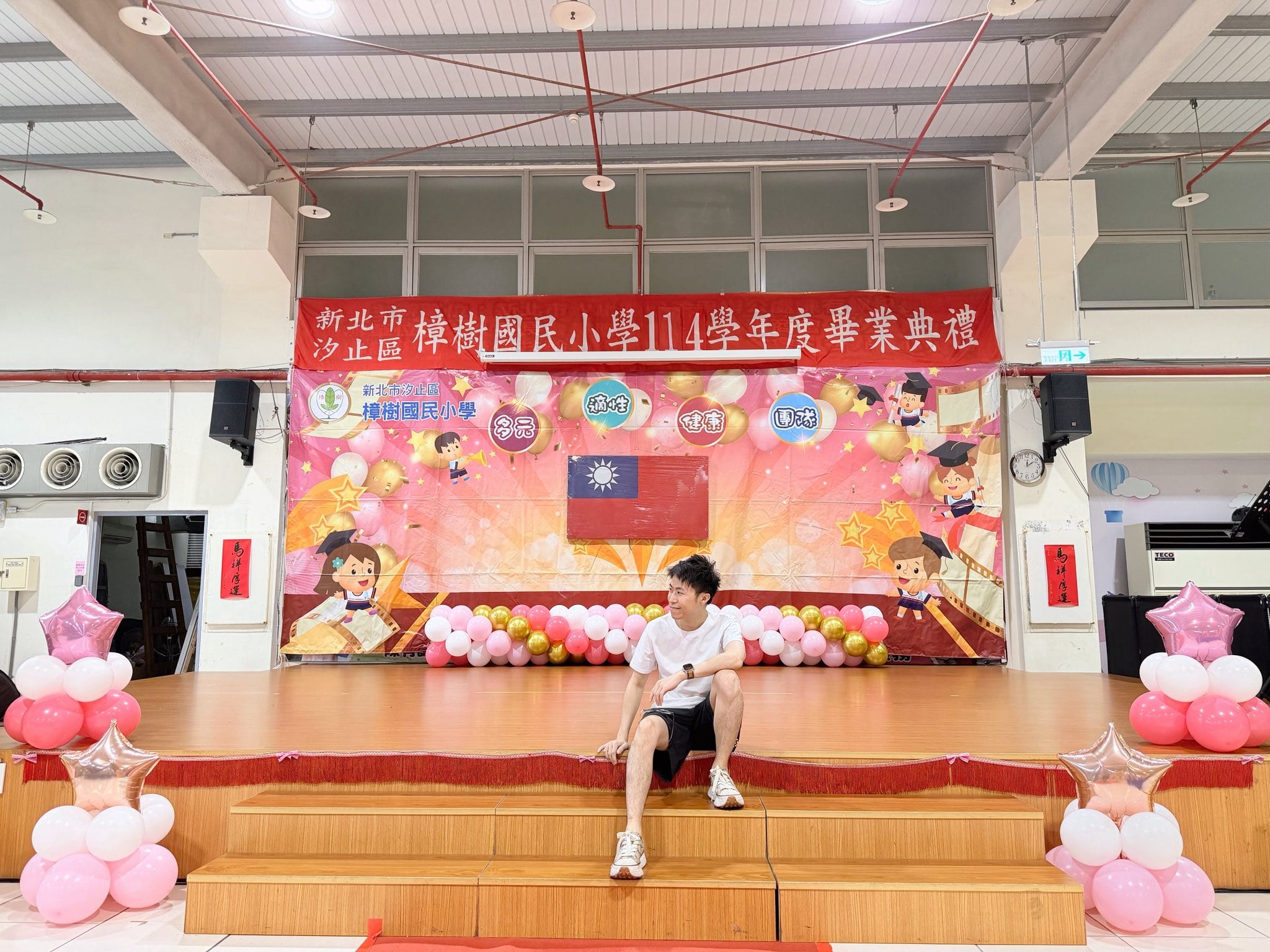 畢業典禮舞台全景,舞台邊緣有粉紅白金氣球串,台下兩側擺放粉紅星星鋁箔氣球柱