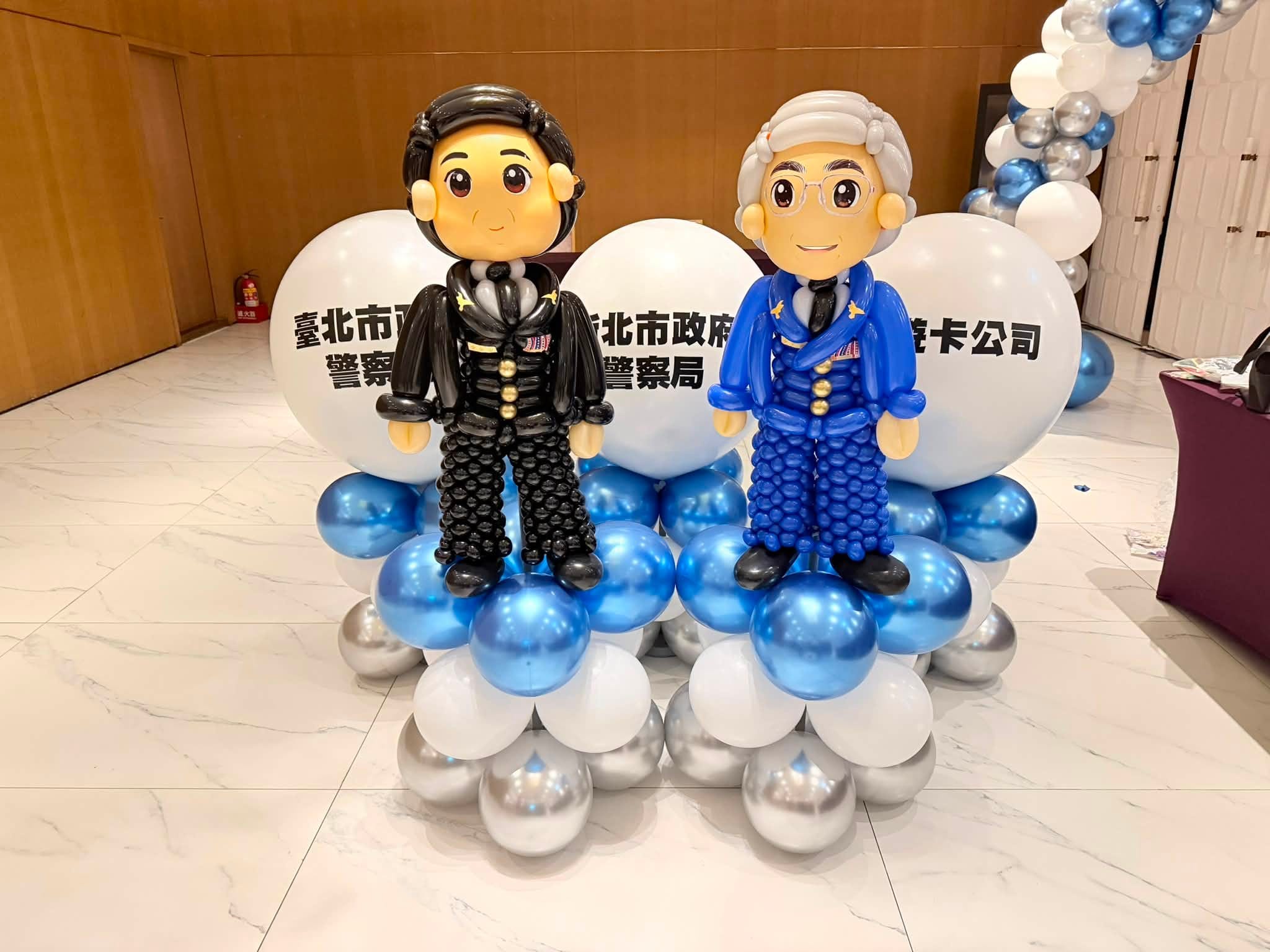 兩尊局長人像氣球站在藍銀白氣球底座上，一尊黑髮穿黑色制服，一尊灰髮戴眼鏡穿藍色制服