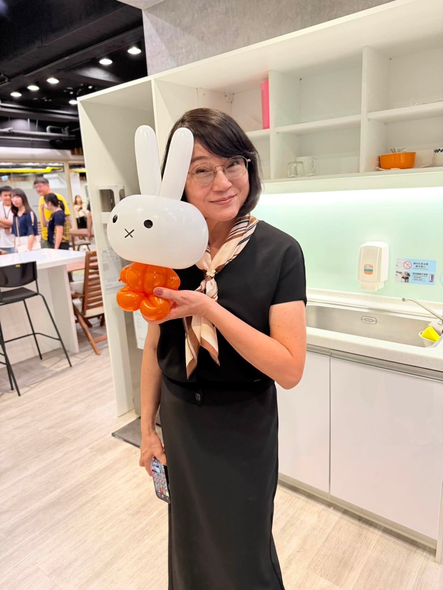 短髮女士把白色兔子造型氣球靠在臉旁,兔子臉上是 X 形嘴巴、身體是橘色