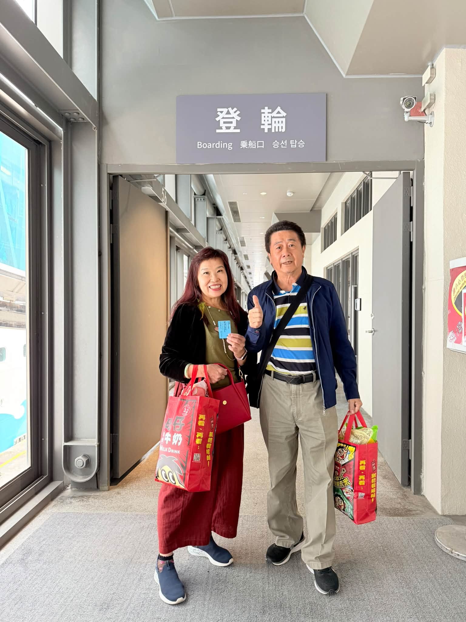 爸媽提著購物袋站在郵輪登輪通道前合影